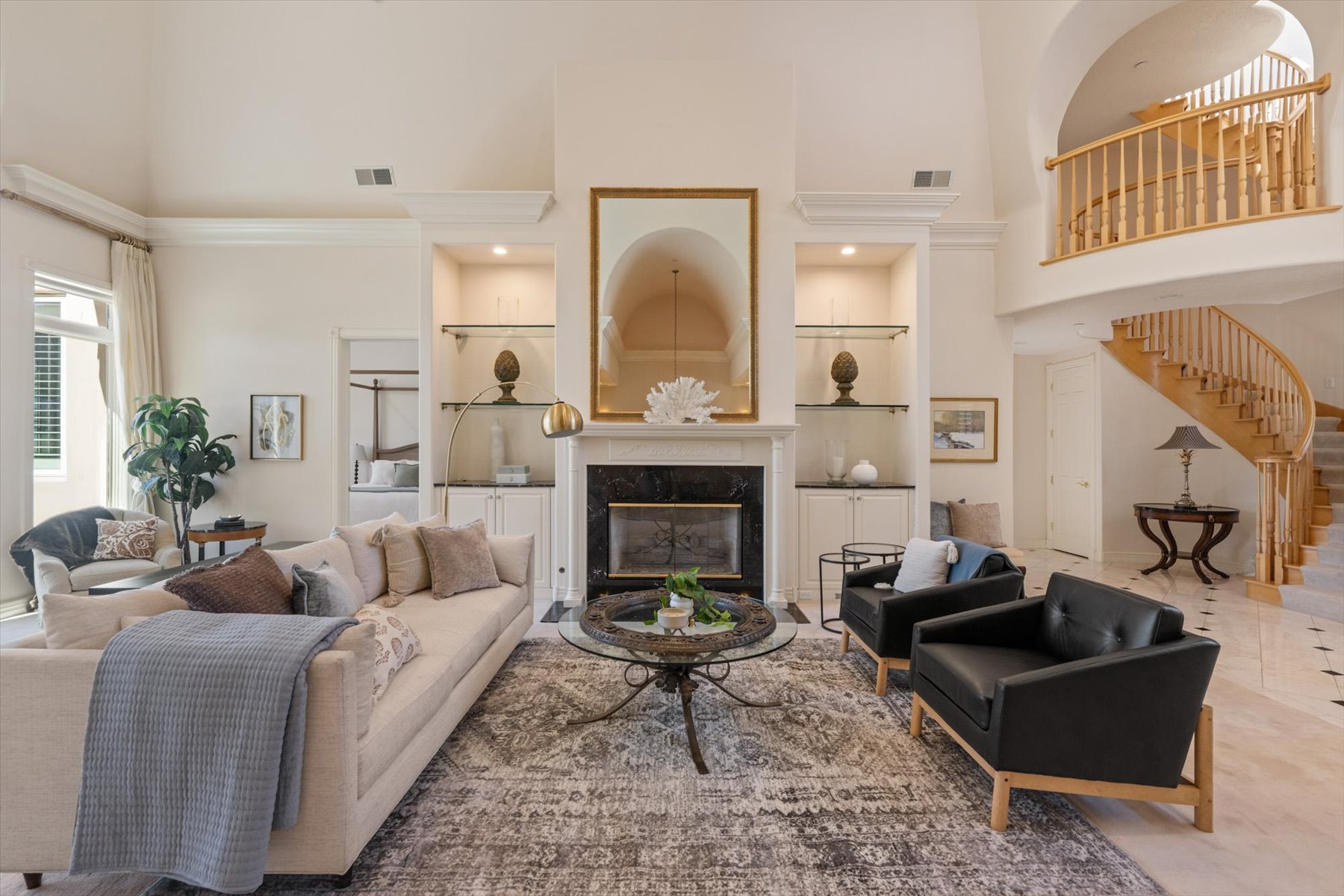 Spacious living area featuring a double-height ceiling, a fireplace with a dark stone surround and white mantel, and built-in shelving with integrated lighting
