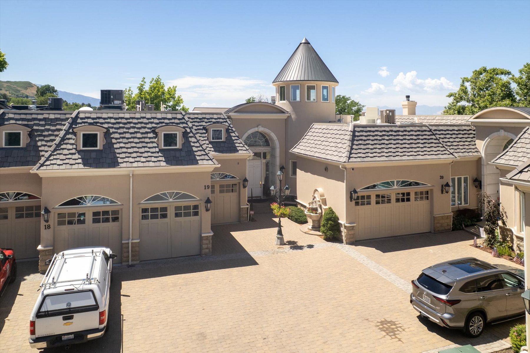 Stucco exterior featuring multiple garage doors with arched transom windows, a distinctive turret, and a paver driveway
