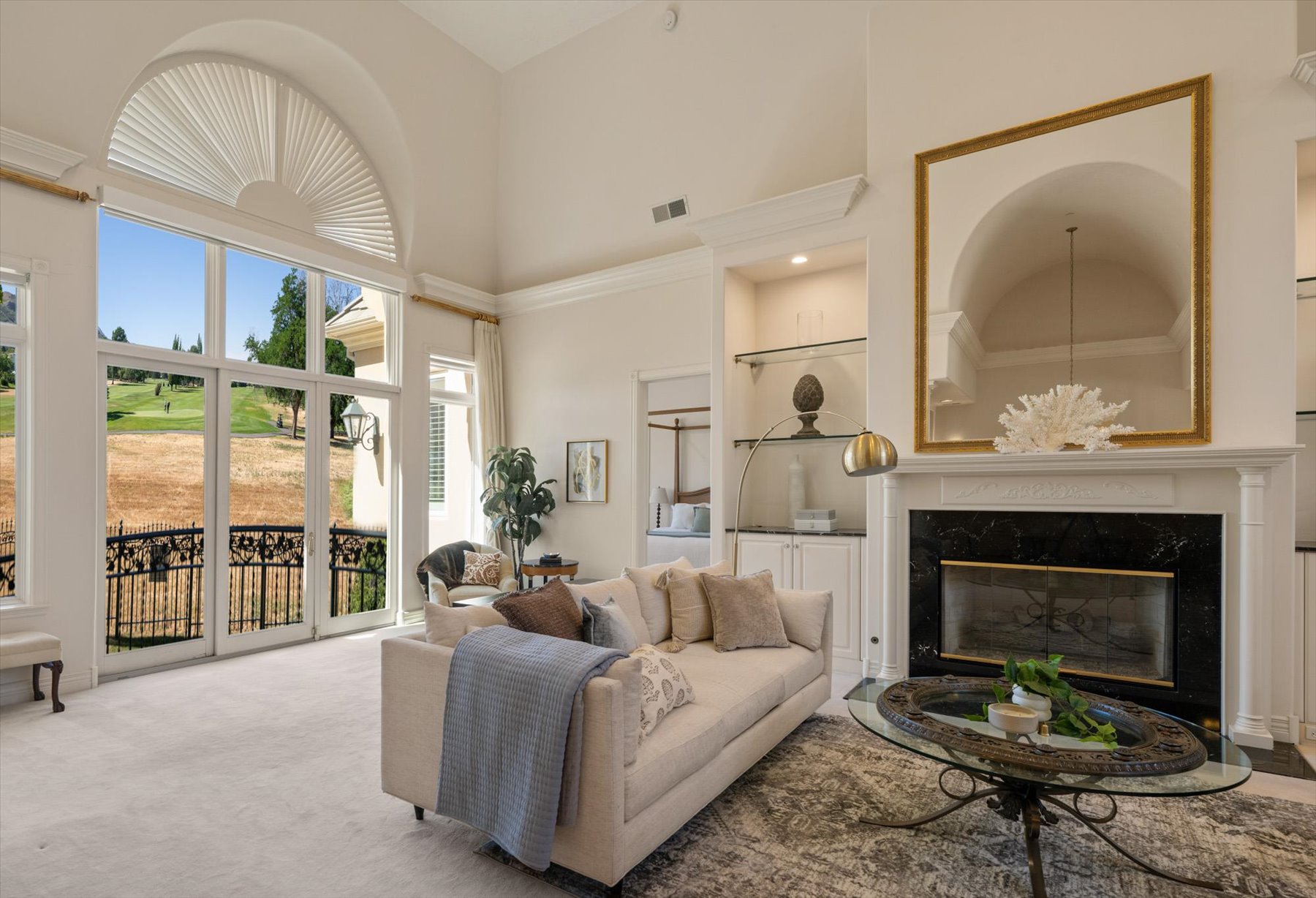 Living space featuring a tall ceiling, a large arched window, and French doors opening to a balcony with an ornate iron railing