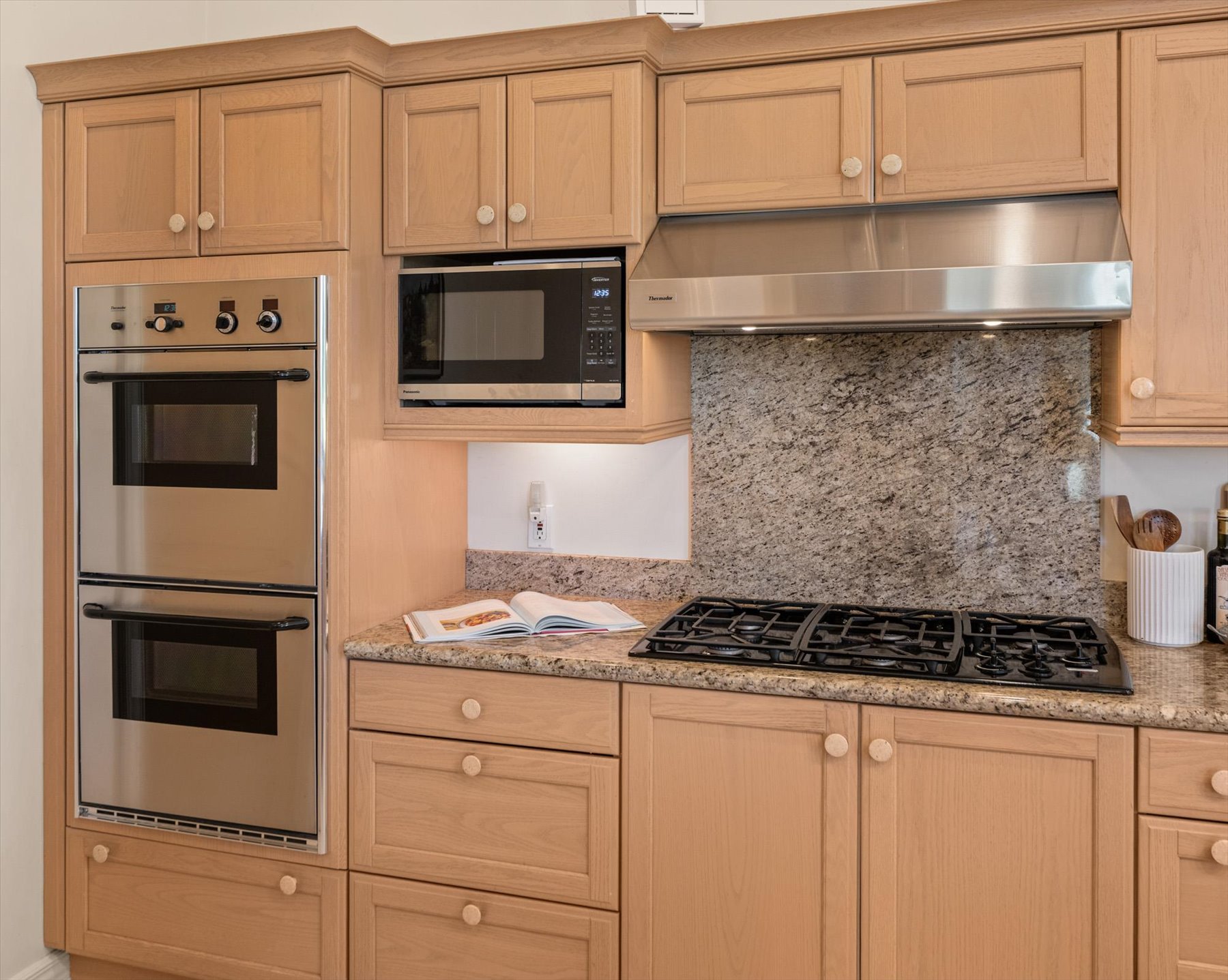 Kitchen featuring light wood cabinetry, stainless steel wall oven and warming oven, a built-in microwave, a gas cooktop, and granite countertops with a matching backsplash