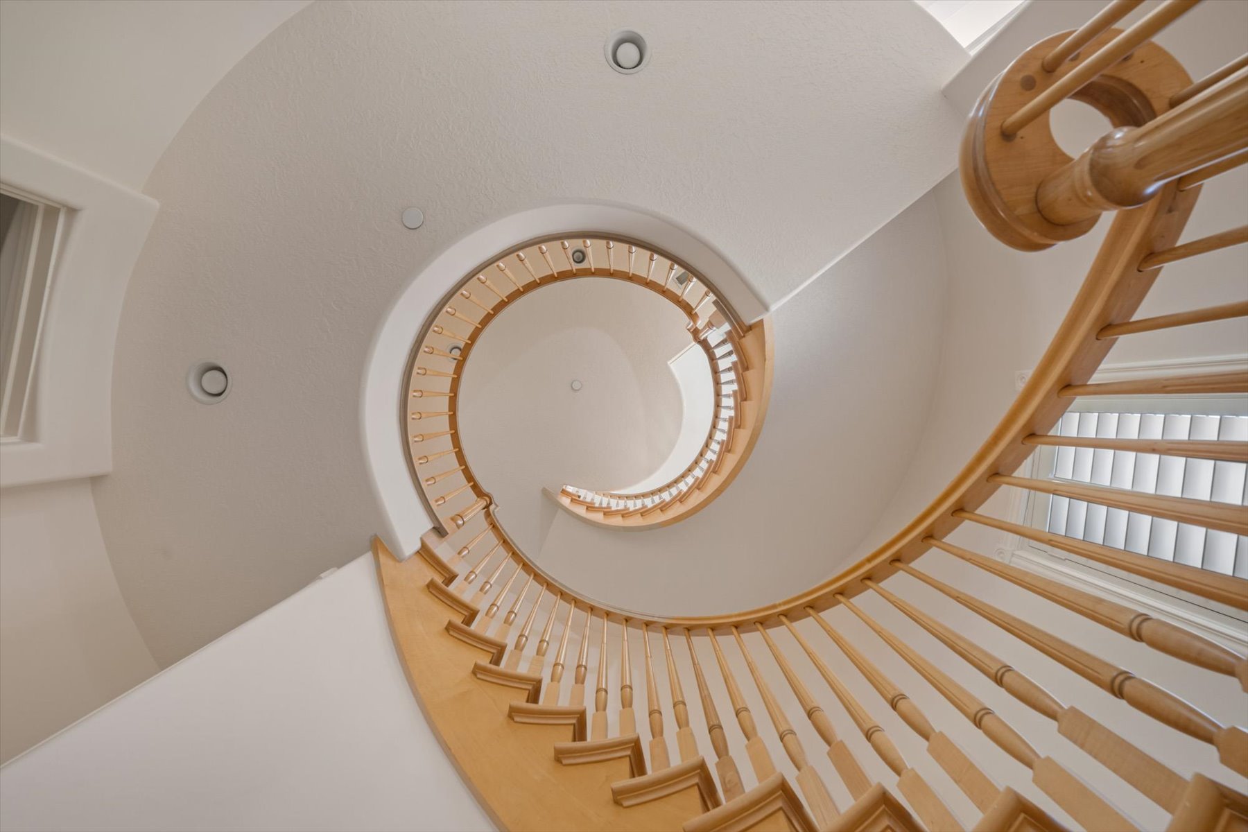 Curved staircase featuring natural wood balusters and handrail, recessed lighting, and  natural illumination