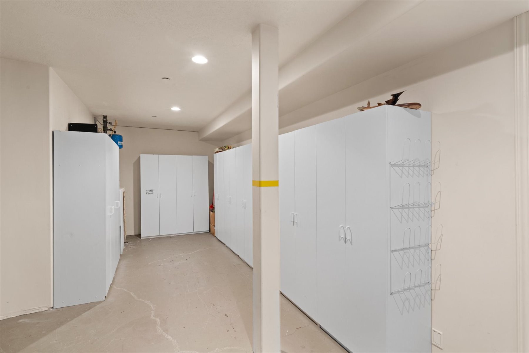 Dedicated storage area featuring multiple white cabinetry units, recessed ceiling lighting, a structural support column, light-toned walls, and concrete flooring
