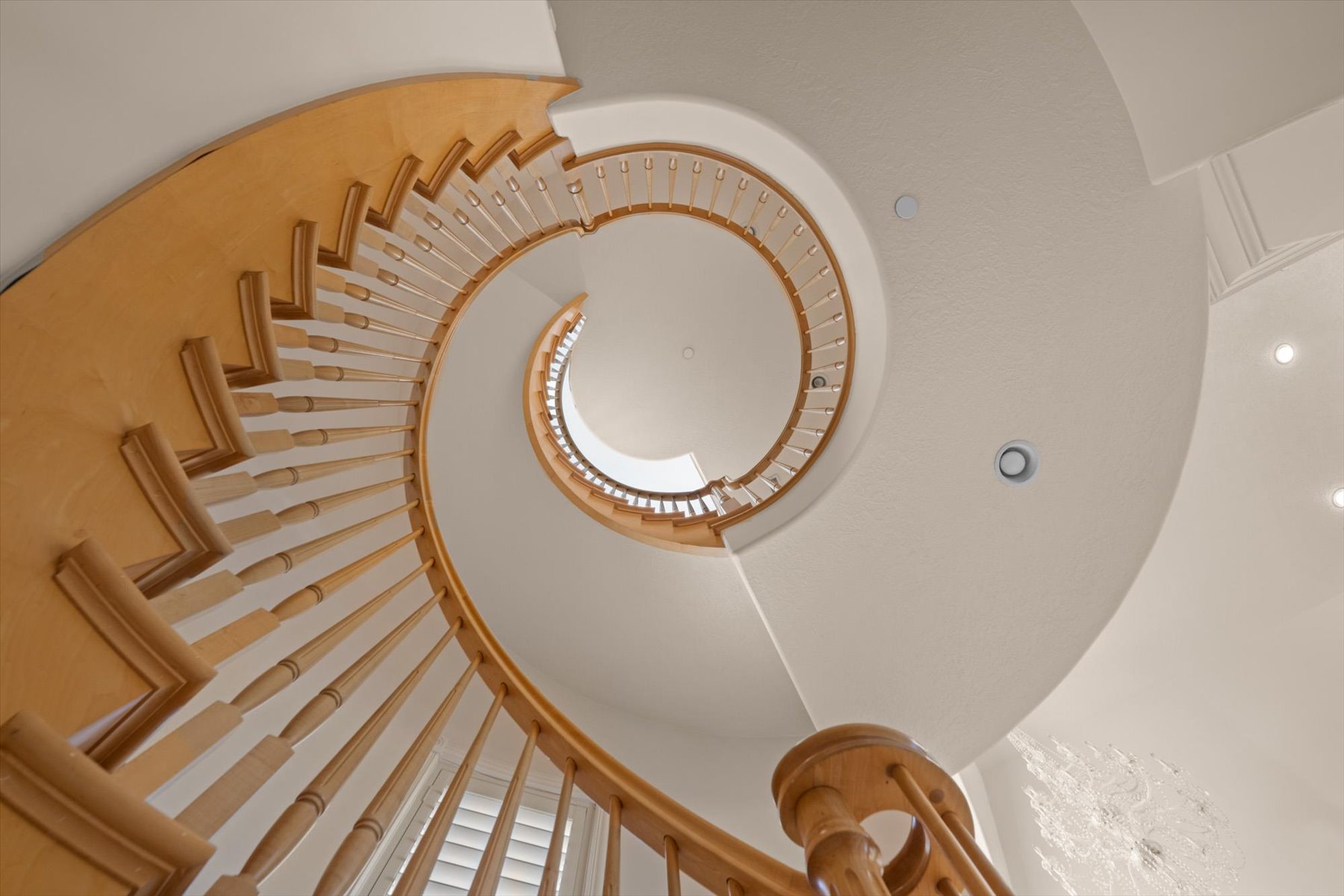 Curving natural wood staircase with balusters, recessed lighting, and white walls