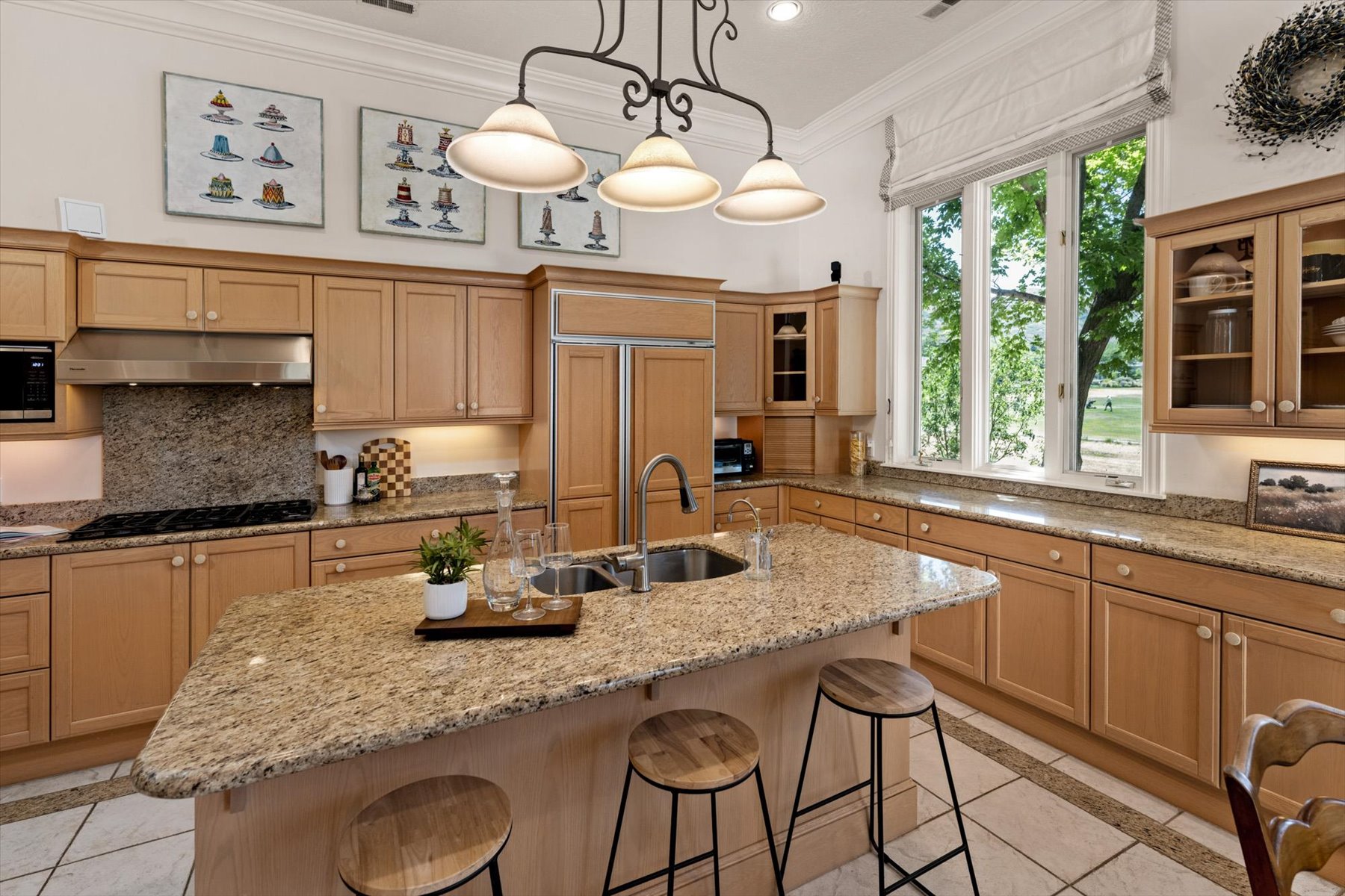 Spacious kitchen featuring an expansive central island with an integrated sink, cabinetry, granite countertops, and a full-height window overlooking exterior grounds