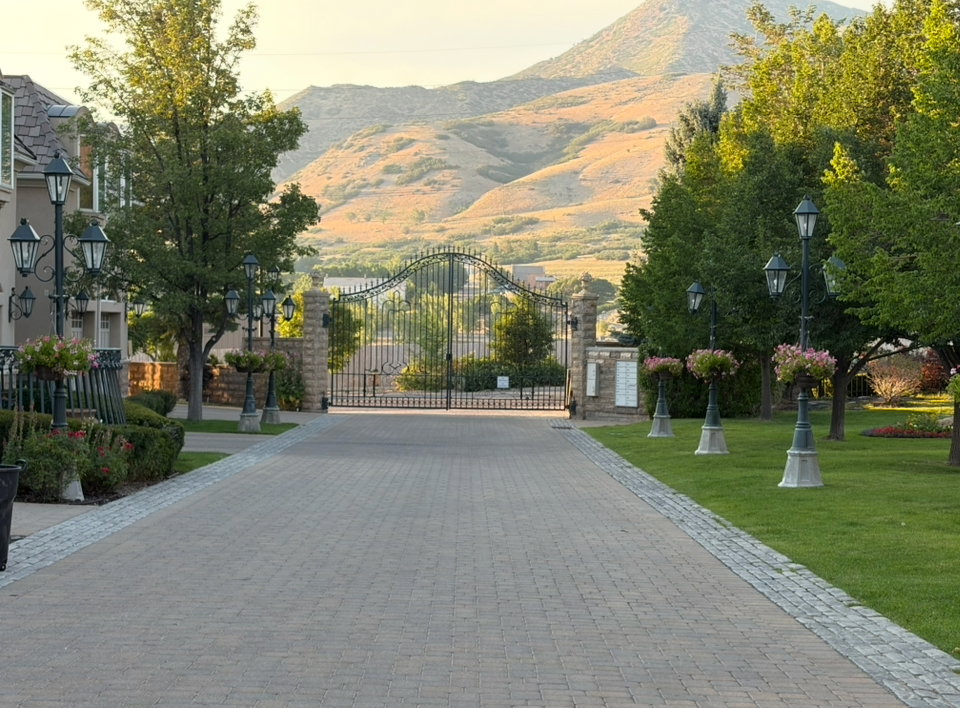 Paver driveway with cobblestone border, flanked by mature trees and manicured lawns