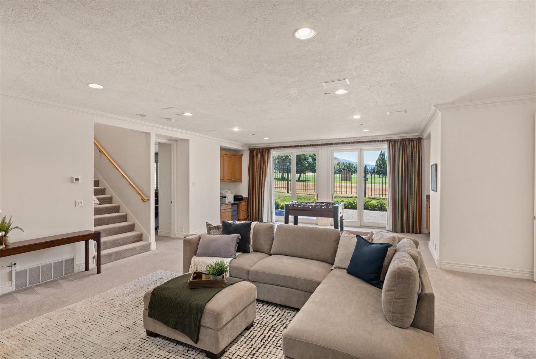 Spacious lower level featuring large sliding glass doors, recessed lighting, carpeted flooring, a built-in wet bar with wood cabinetry, and a carpeted stairway with a wood handrail