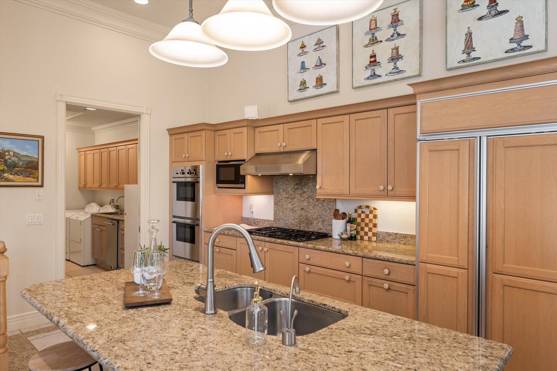 Gourmet kitchen featuring a large island with an undermount sink, granite countertops, wood cabinetry, stainless steel appliances, and high ceilings