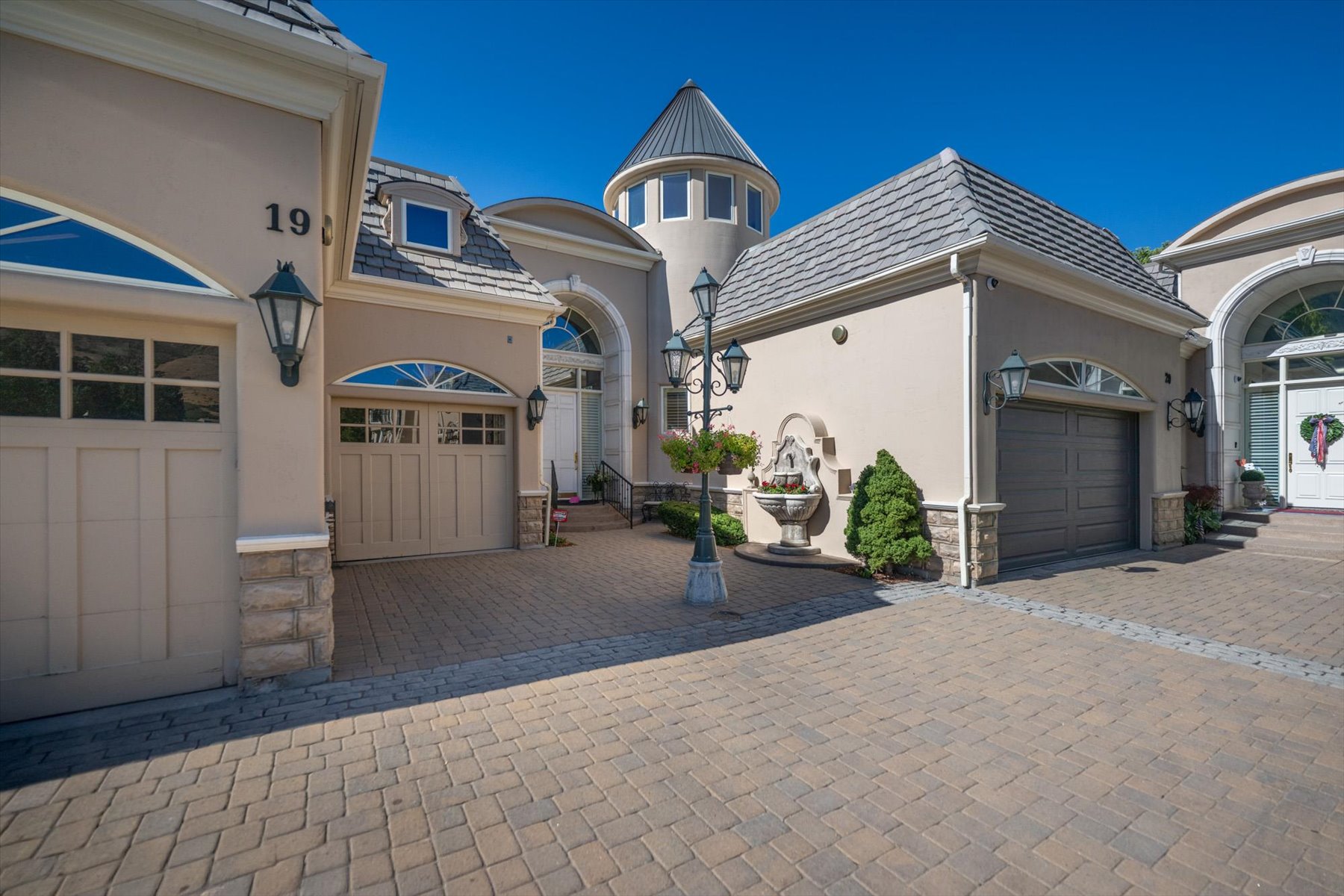 Paver driveway leading to a multi-car garage with arched windows and decorative outdoor lighting