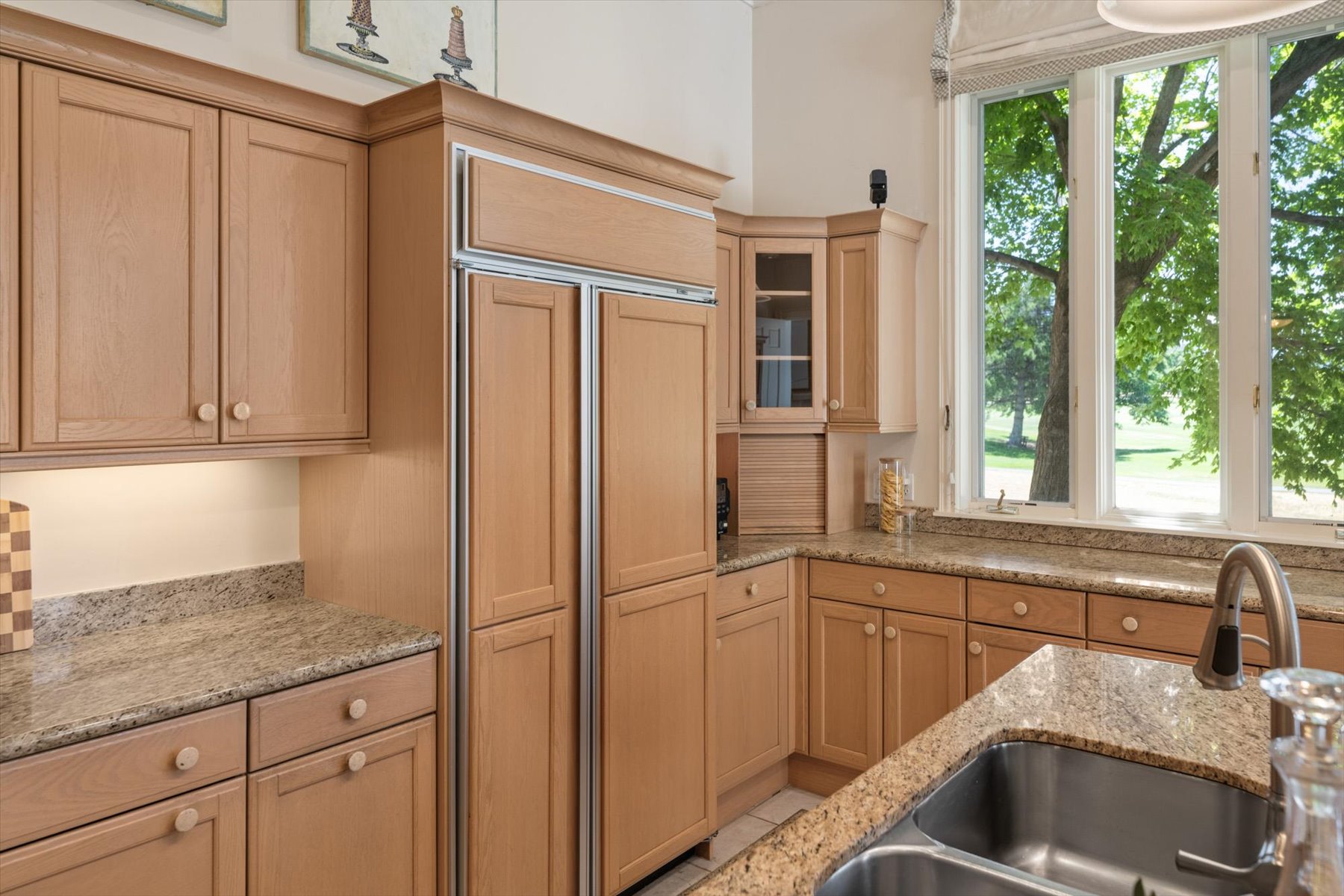 Kitchen featuring wood cabinetry, integrated refrigerator, granite countertops, double basin sink with a gooseneck faucet, and a large multi-pane window