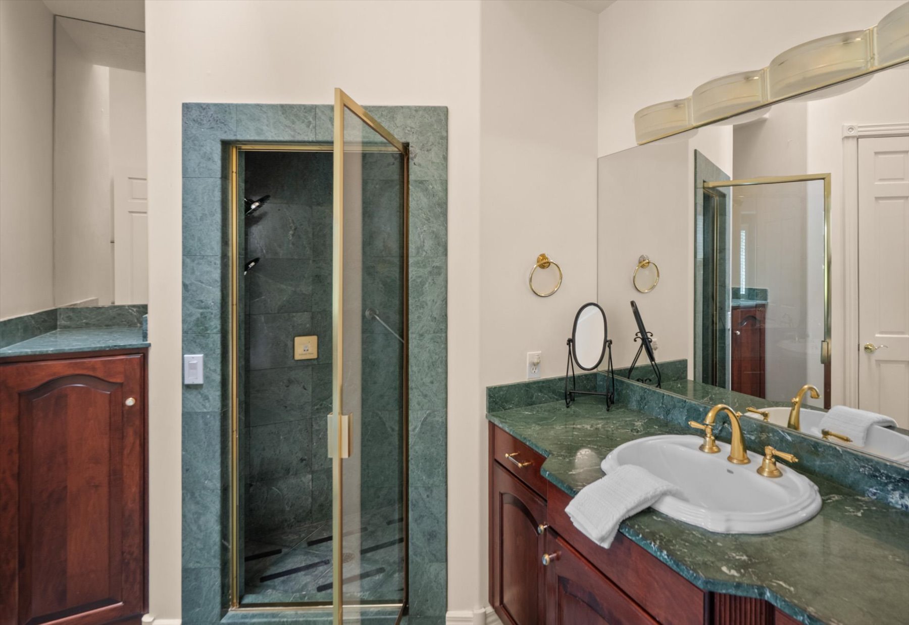 Bathroom featuring a glass-enclosed shower with gold-tone fixtures, a vanity with a green stone countertop, and wood cabinetry