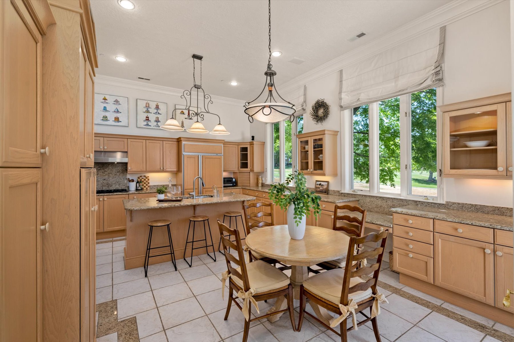 Spacious kitchen featuring extensive light wood cabinetry, white tile flooring, granite countertops, and large windows