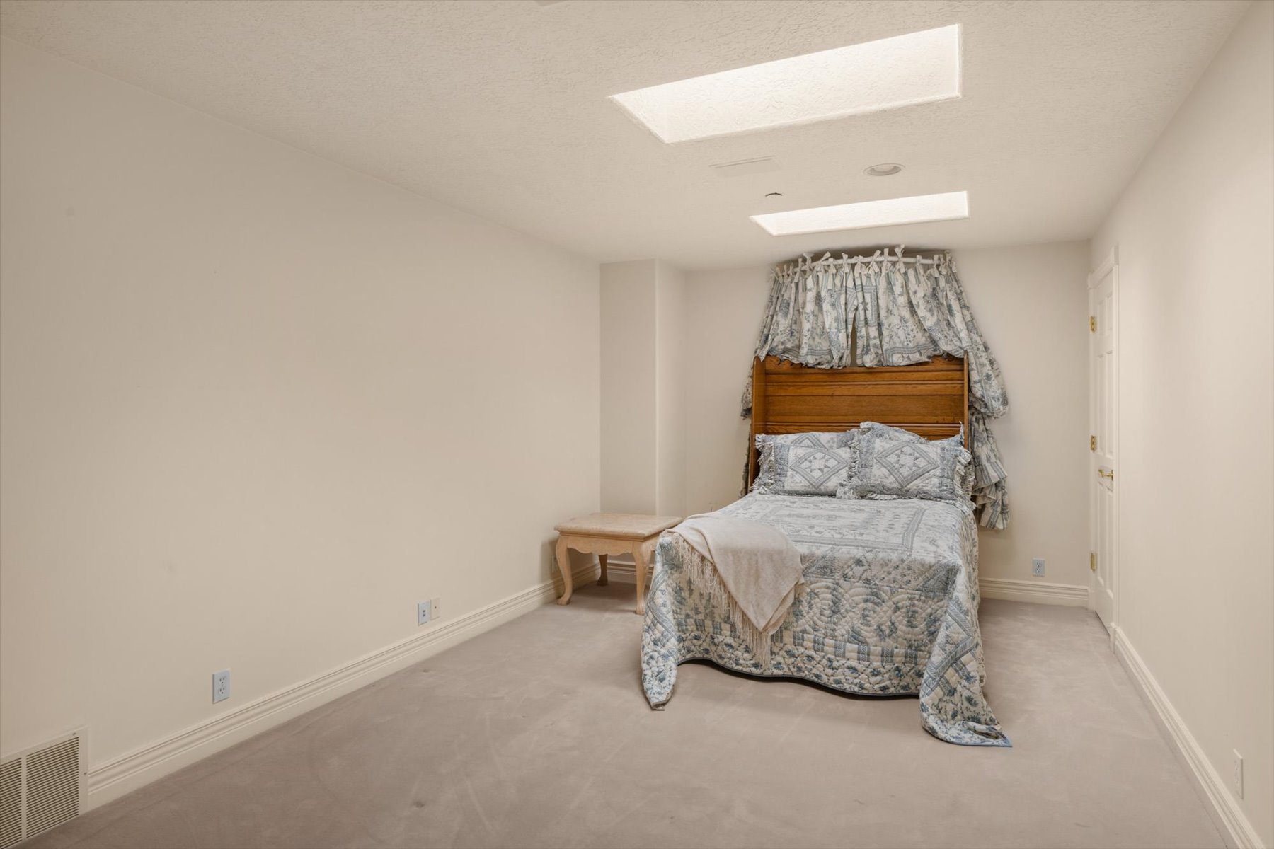 Recessed lighting and ceiling skylights illuminate a room featuring soft carpeting and white baseboards
