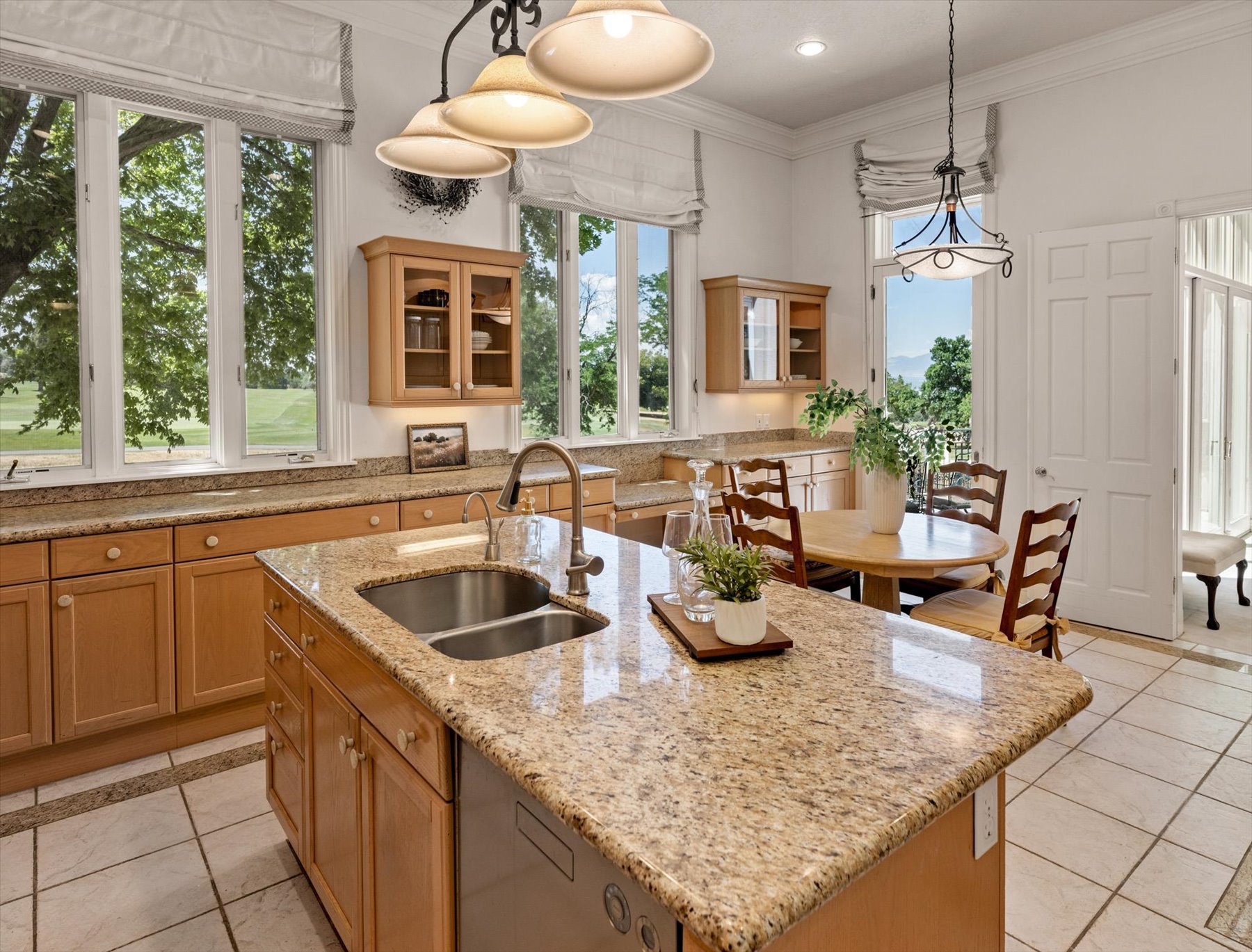 Kitchen featuring an expansive island with a dual basin sink, light-toned cabinetry, granite countertops, tile flooring, and multiple large windows looking out to Bonneville Golf Course