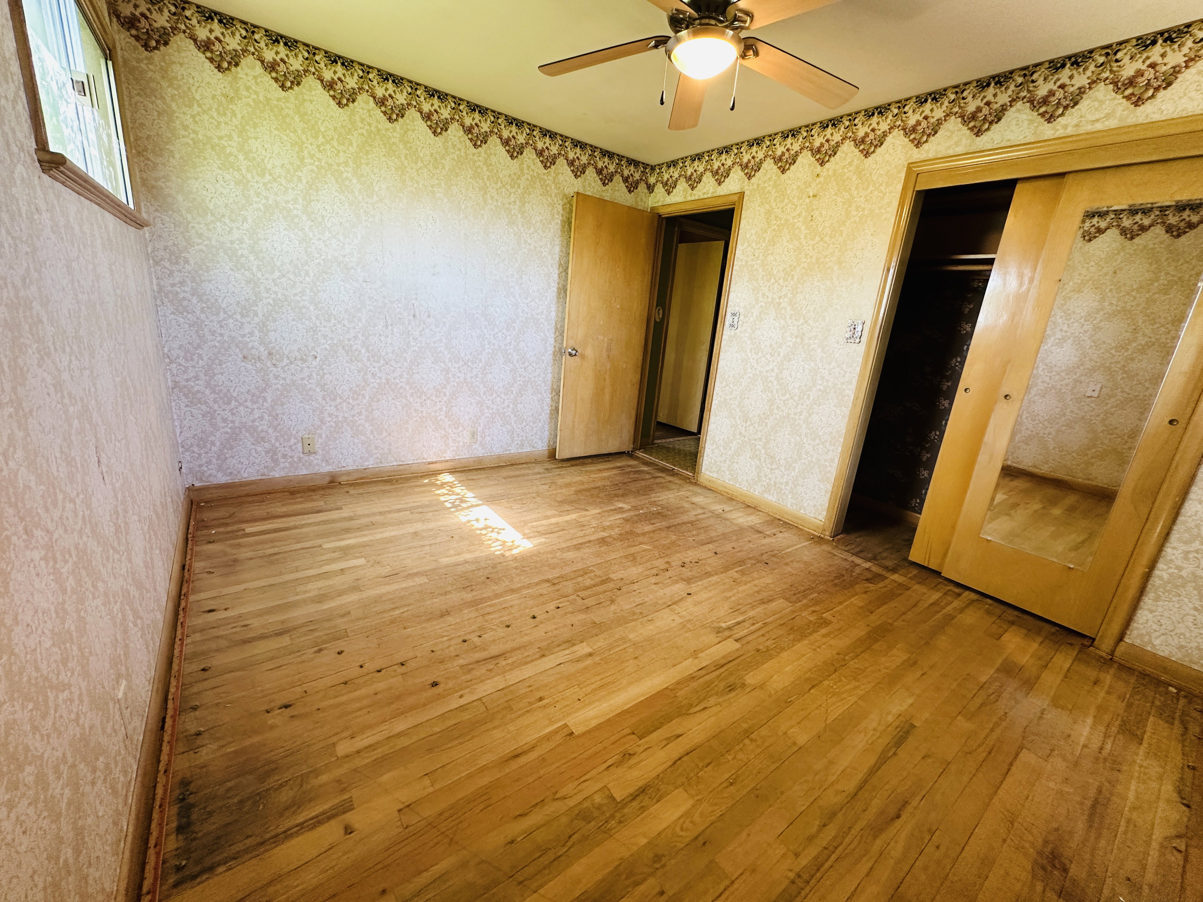 Room featuring wood-finish flooring, a ceiling fan with integrated lighting, and a window with wood trim