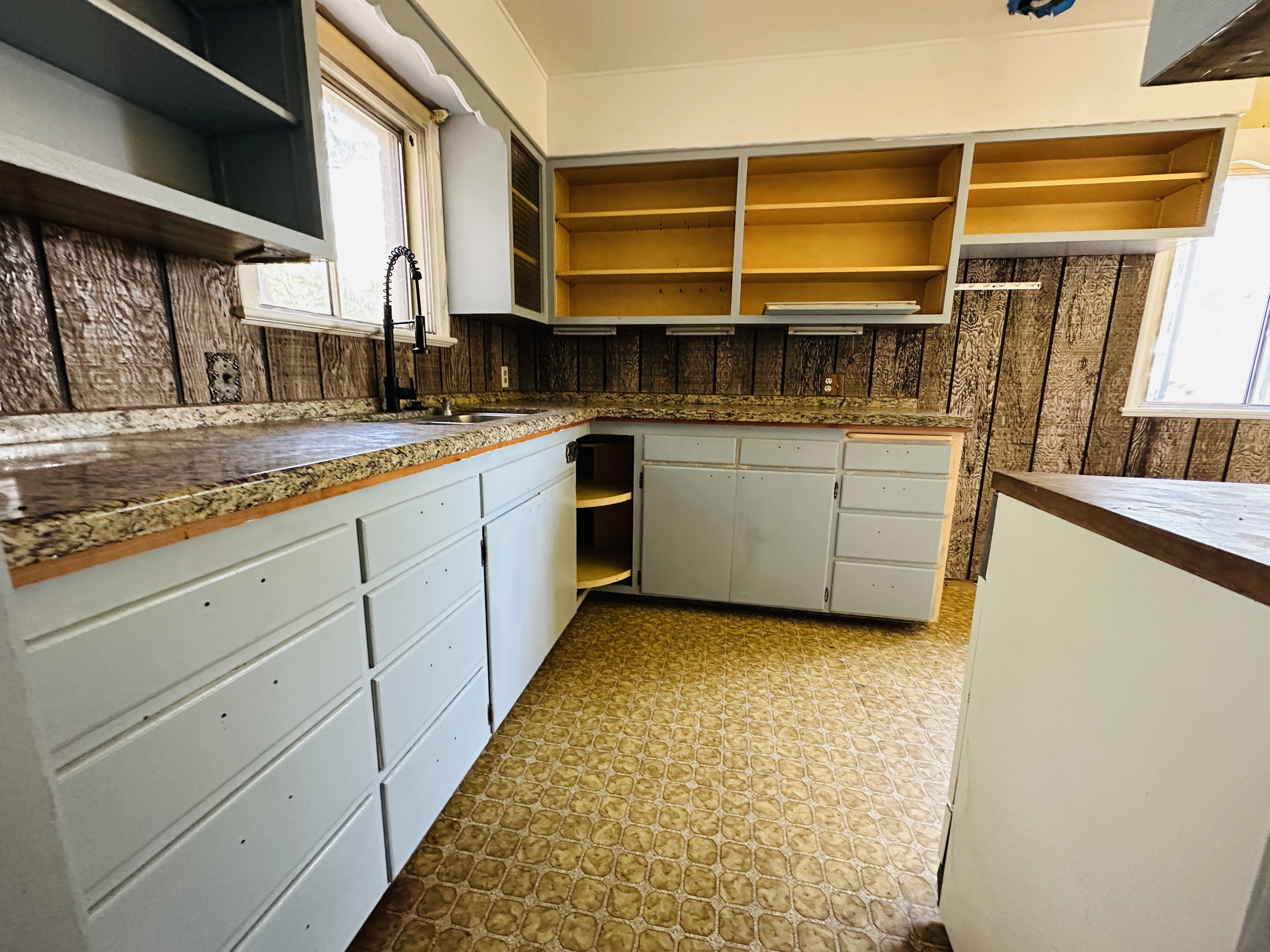 Kitchen featuring light blue lower cabinetry, open upper shelving, patterned flooring, and a dark wood-finish backsplash
