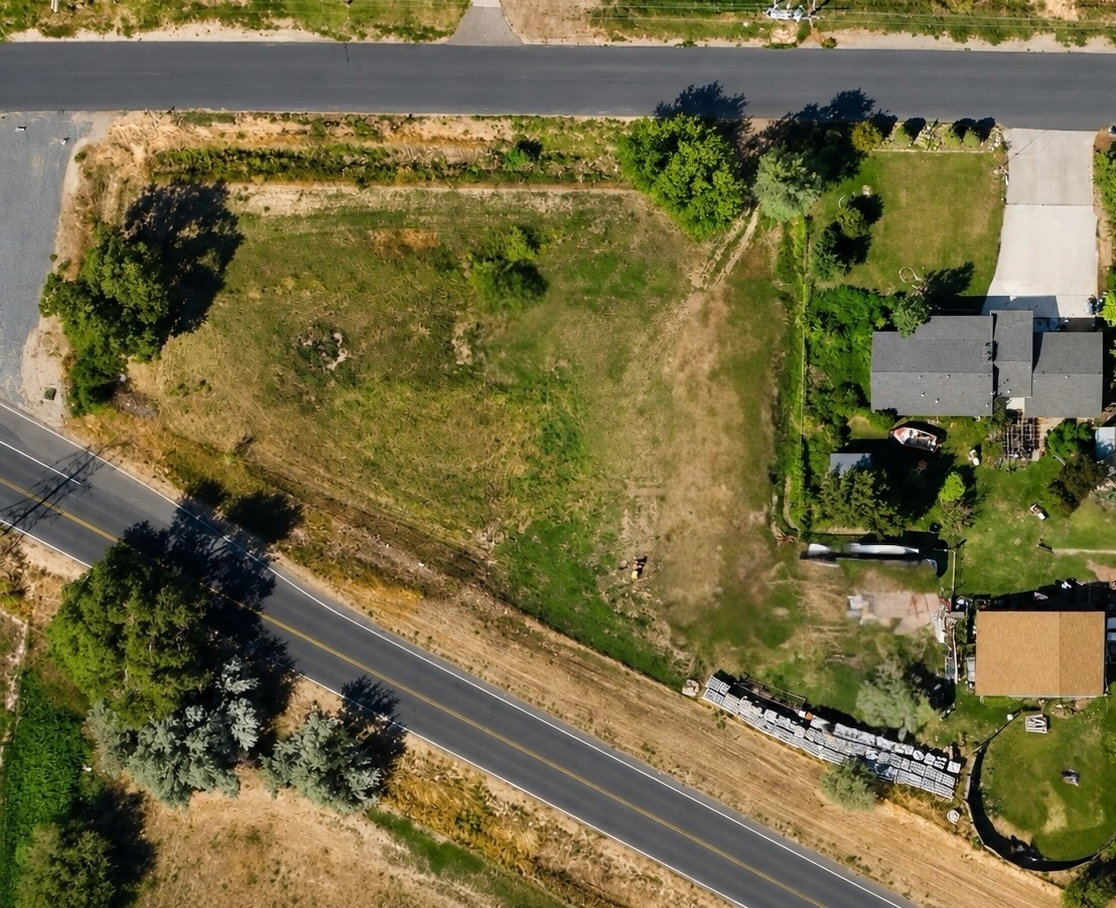 Expansive undeveloped parcel featuring mature trees, a partially paved road frontage, and a gravel perimeter