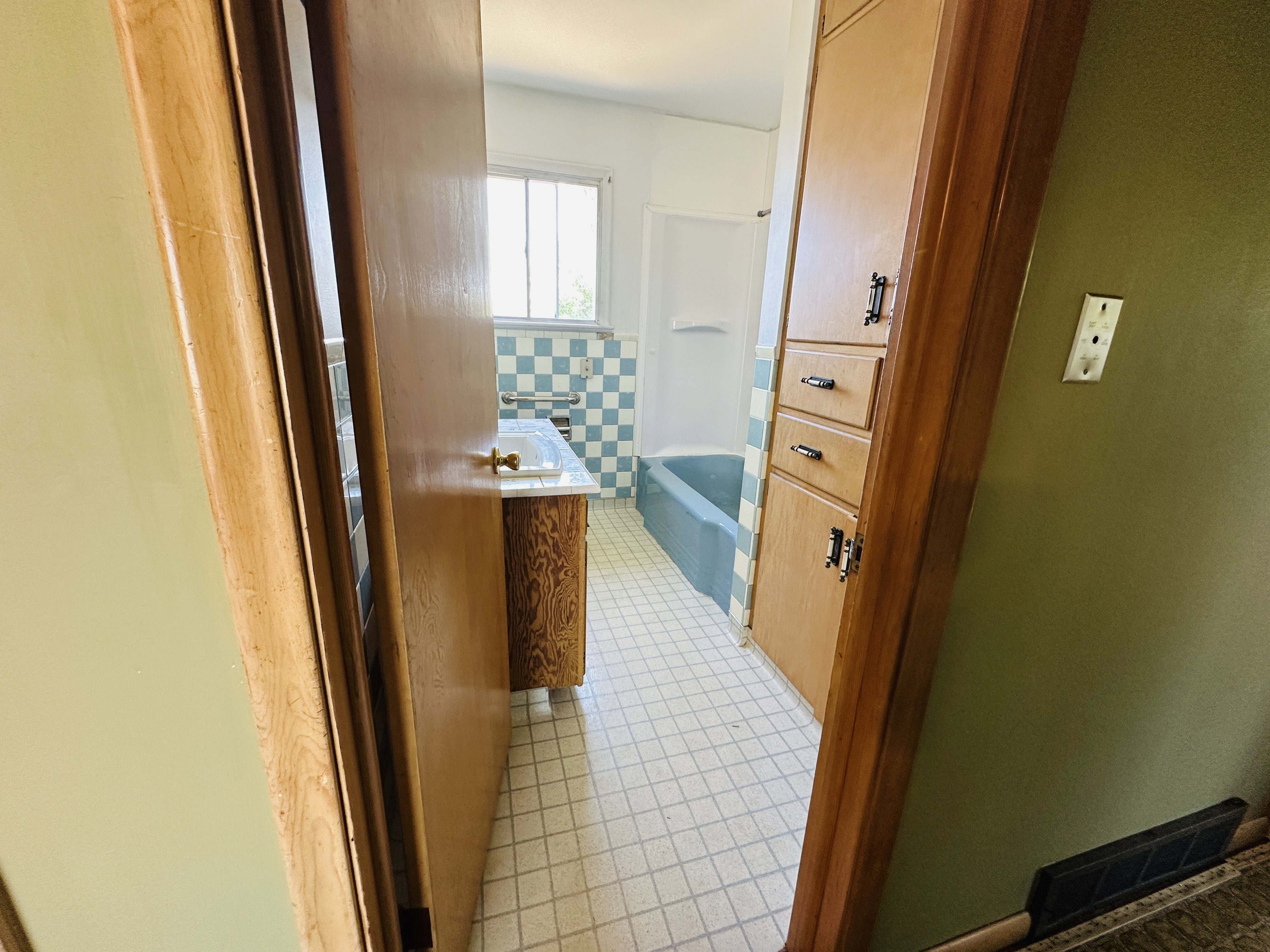 Bathroom featuring a vanity with a white countertop and brass-toned faucet, blue and white checkered wall tiling, a built-in bathtub with blue side paneling, and wood-finish storage cabinetry