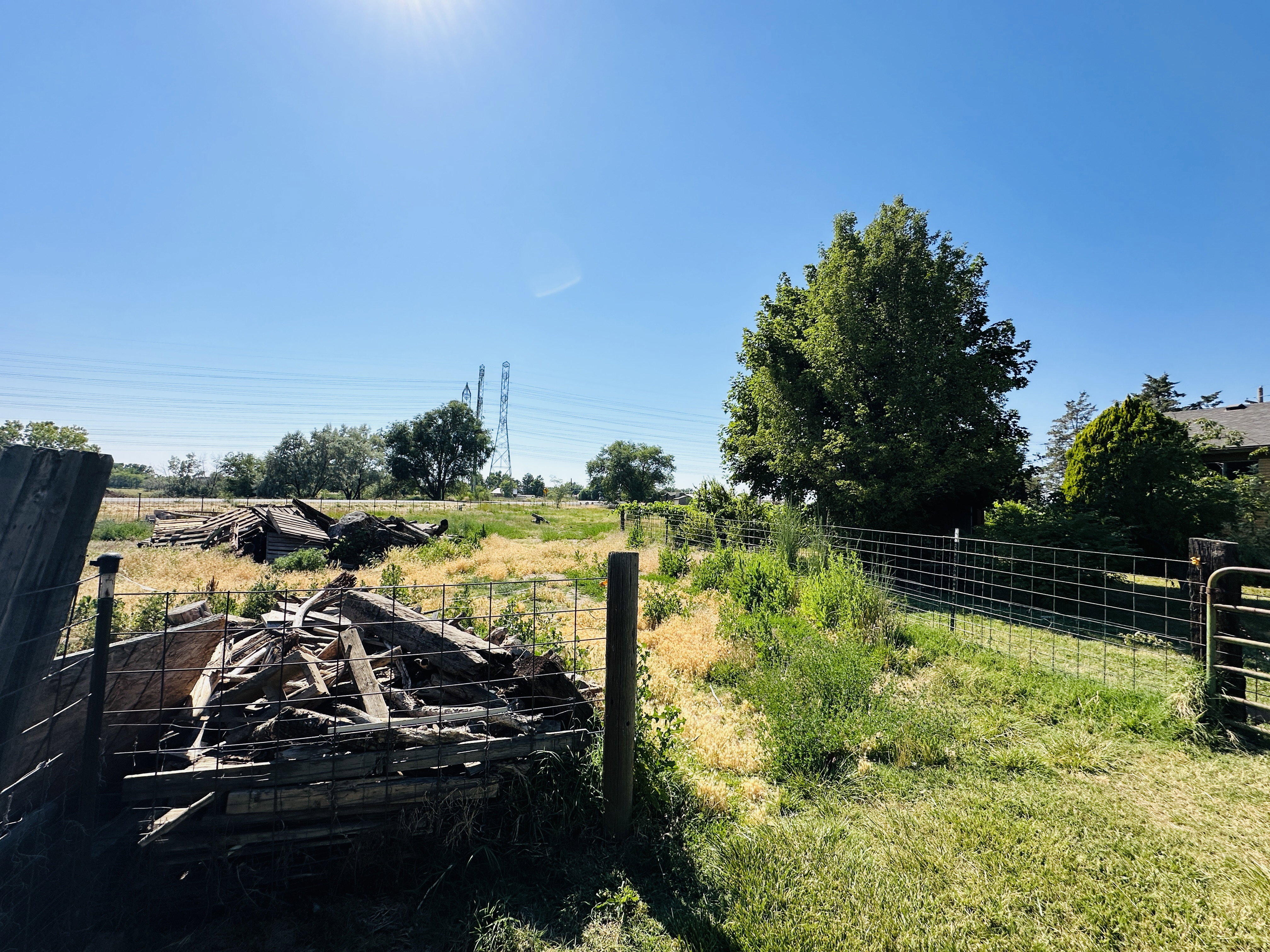 Expansive open land featuring a wire fence, mature trees, and a clear sky