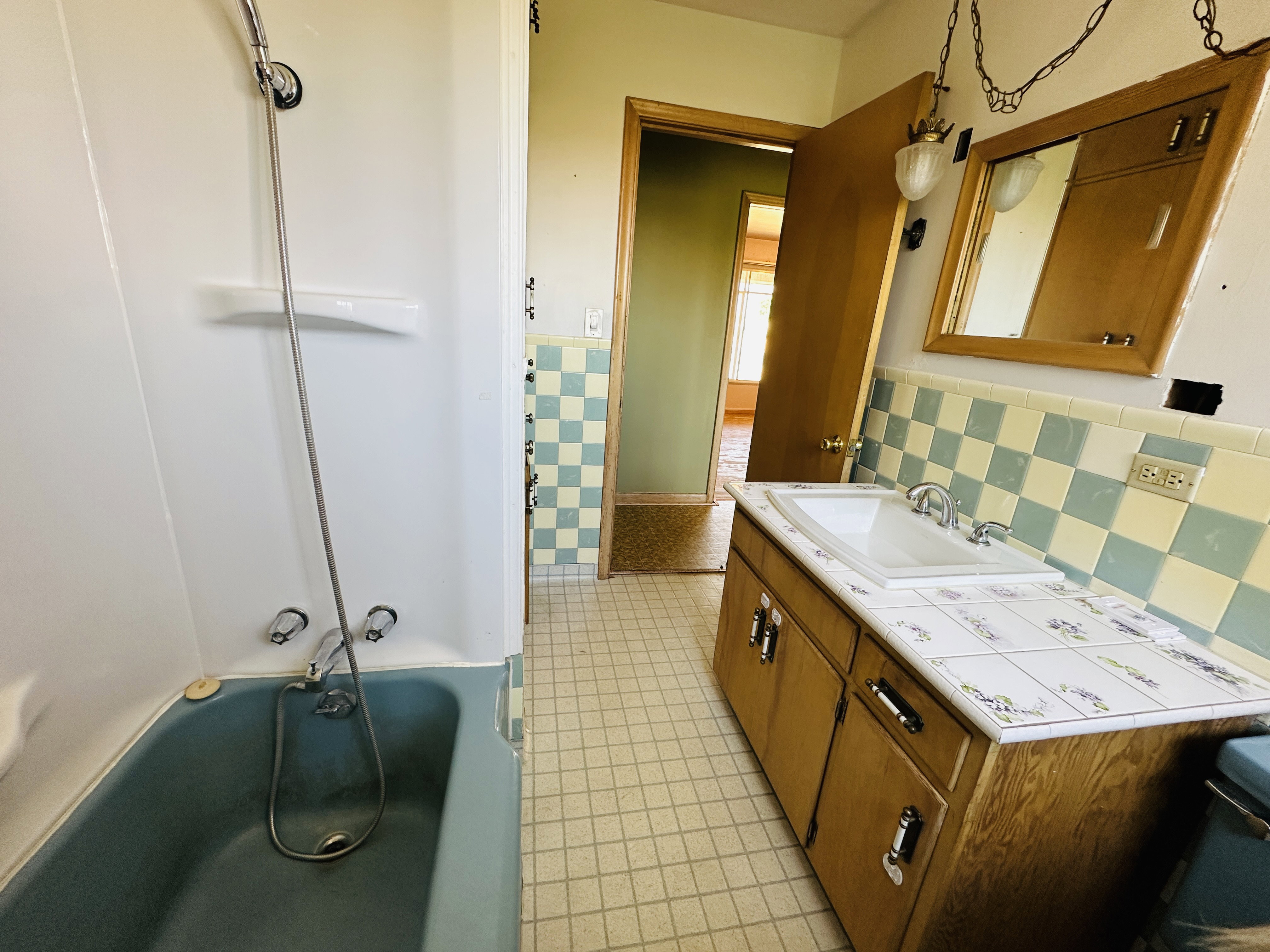 Bathroom featuring a light blue bathtub with a white shower surround, a wood-finish vanity with a tiled countertop, a white drop-in sink, and a mirrored medicine cabinet