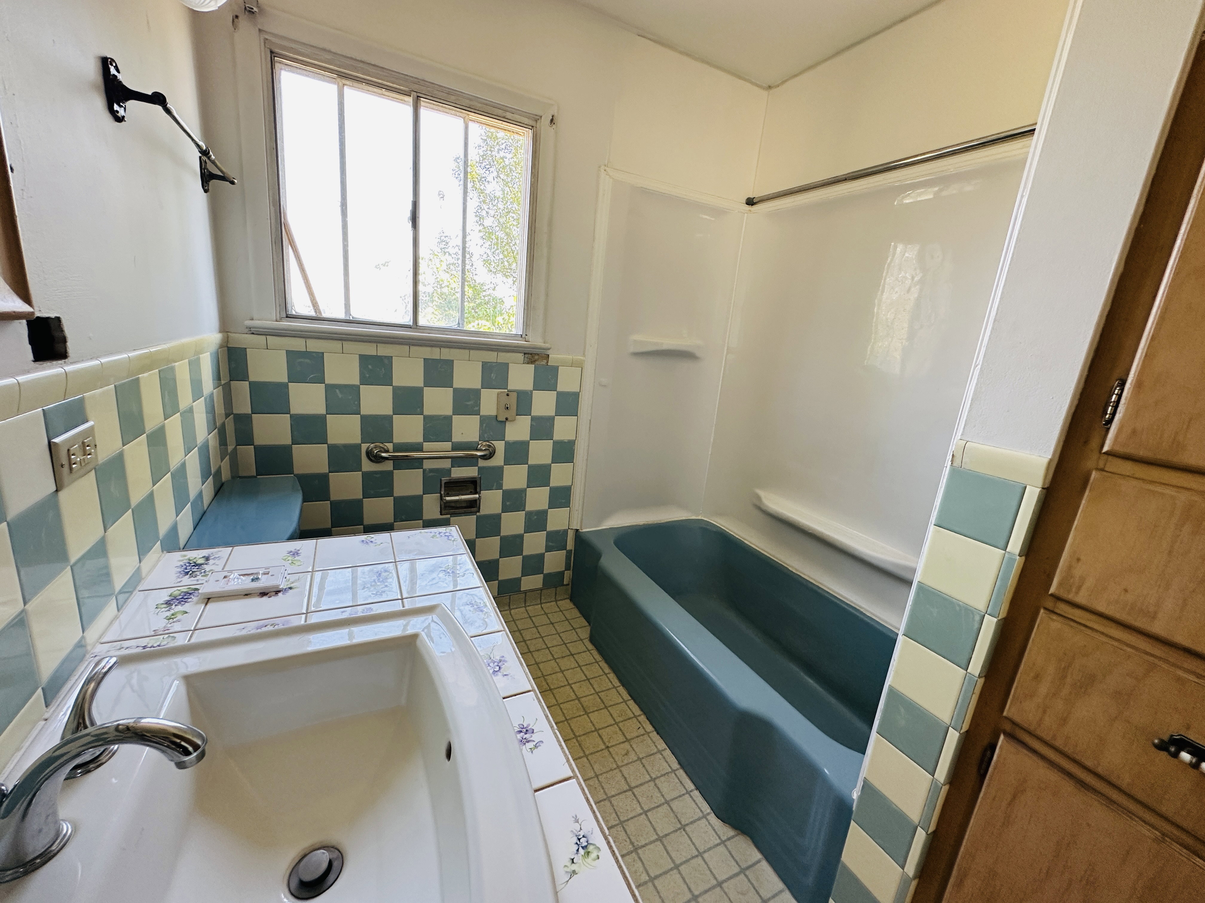 Bathroom featuring a blue bathtub, white shower surround, and checkerboard wall tiling