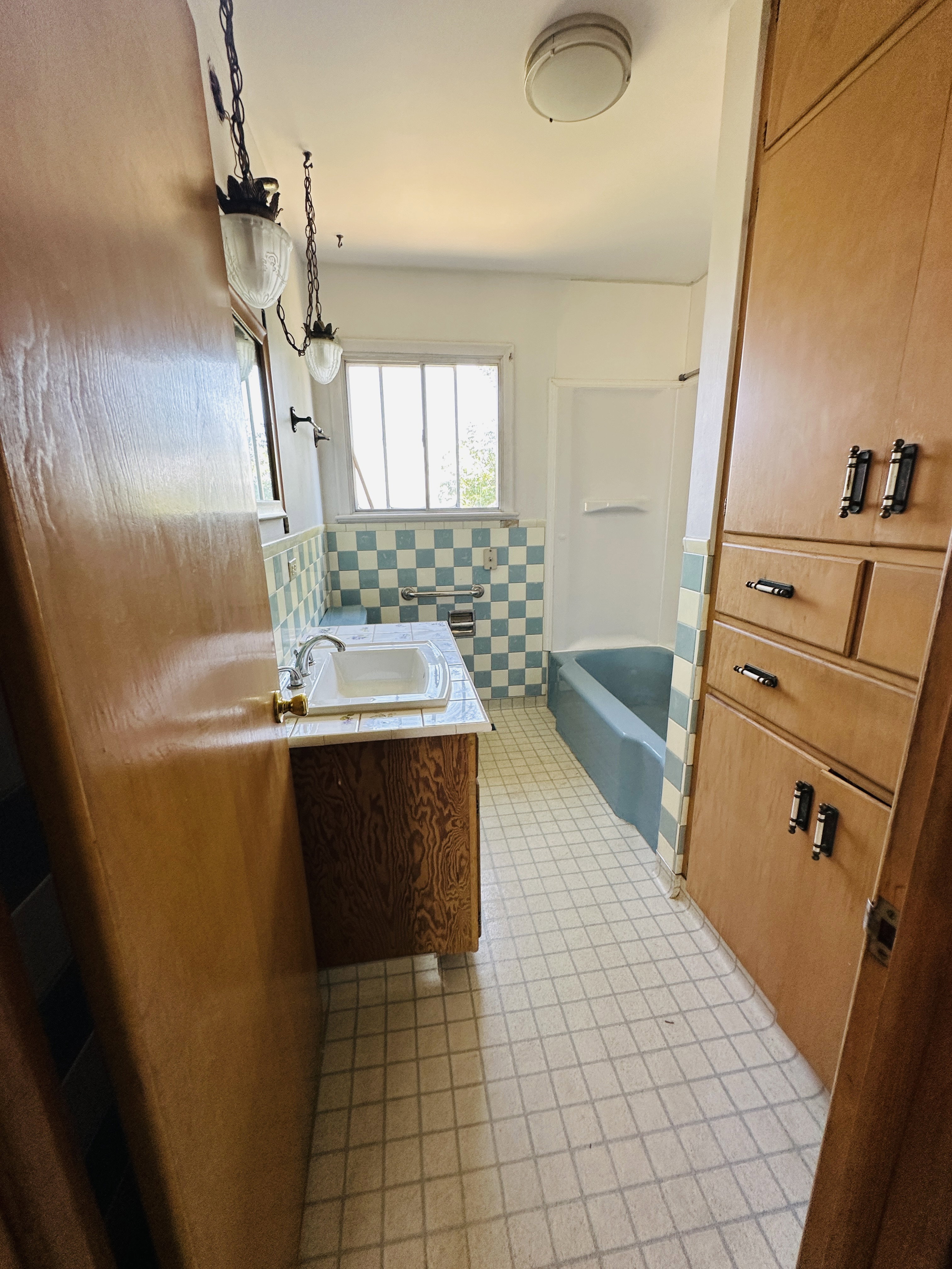 Bathroom featuring a built-in bathtub, a window with multiple panes, and checkered wall tiling