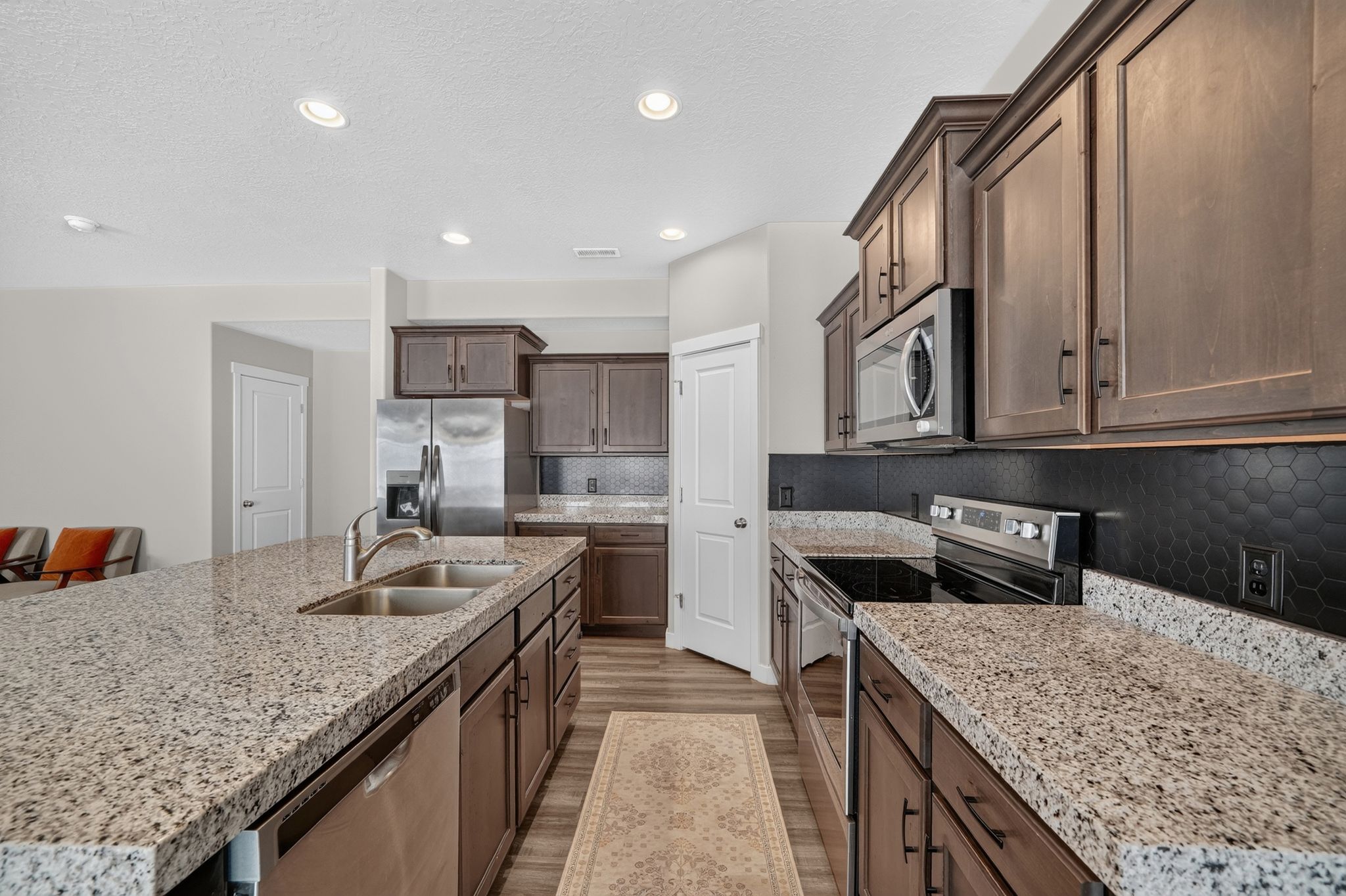 Kitchen featuring granite countertops, wood-finish flooring, dark wood cabinetry, a stainless steel double-basin sink, and a black honeycomb tile backsplash