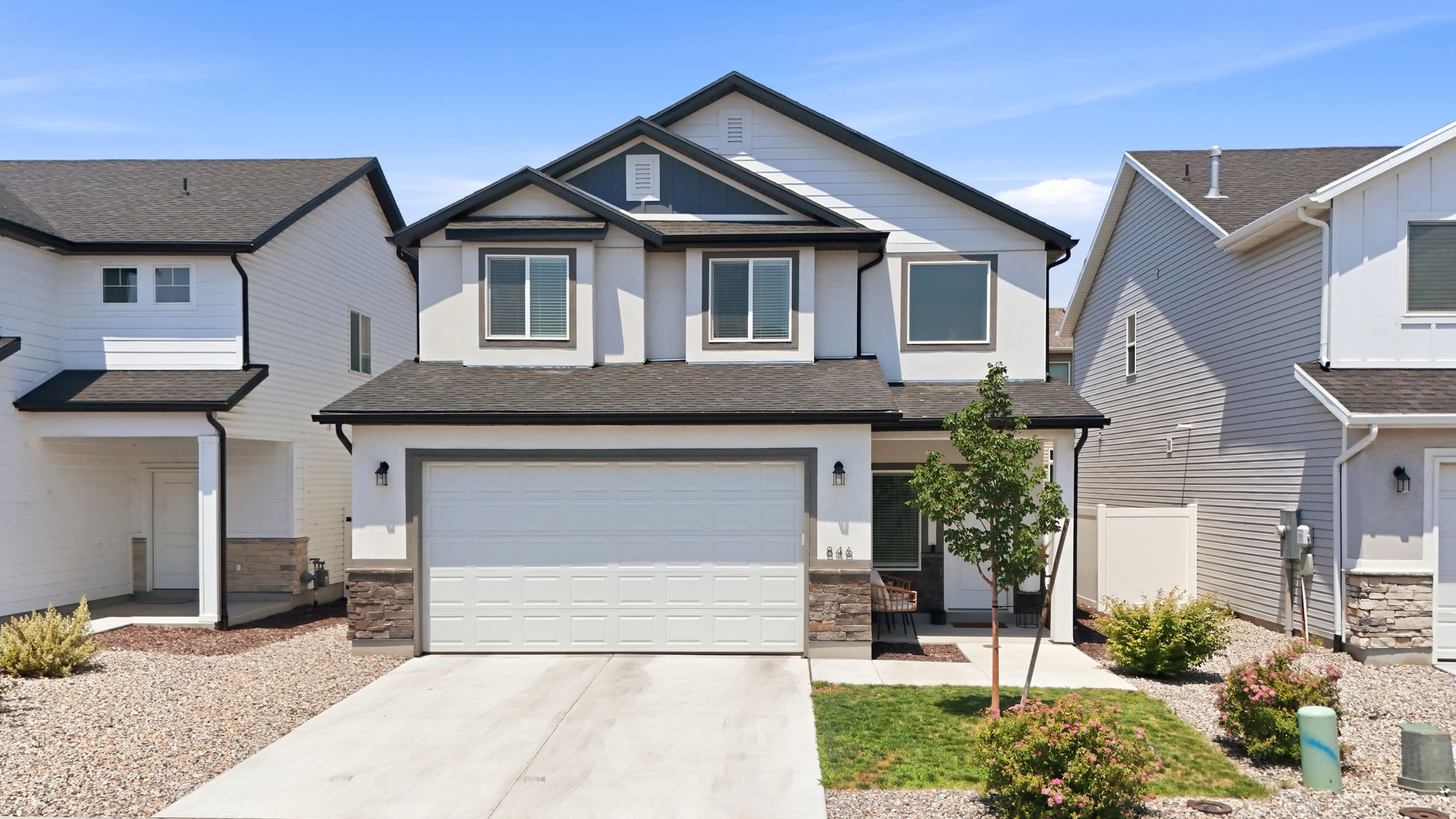 Contemporary two-story residence featuring a two-car garage, dark shingle roof, and stucco exterior with stone veneer accents