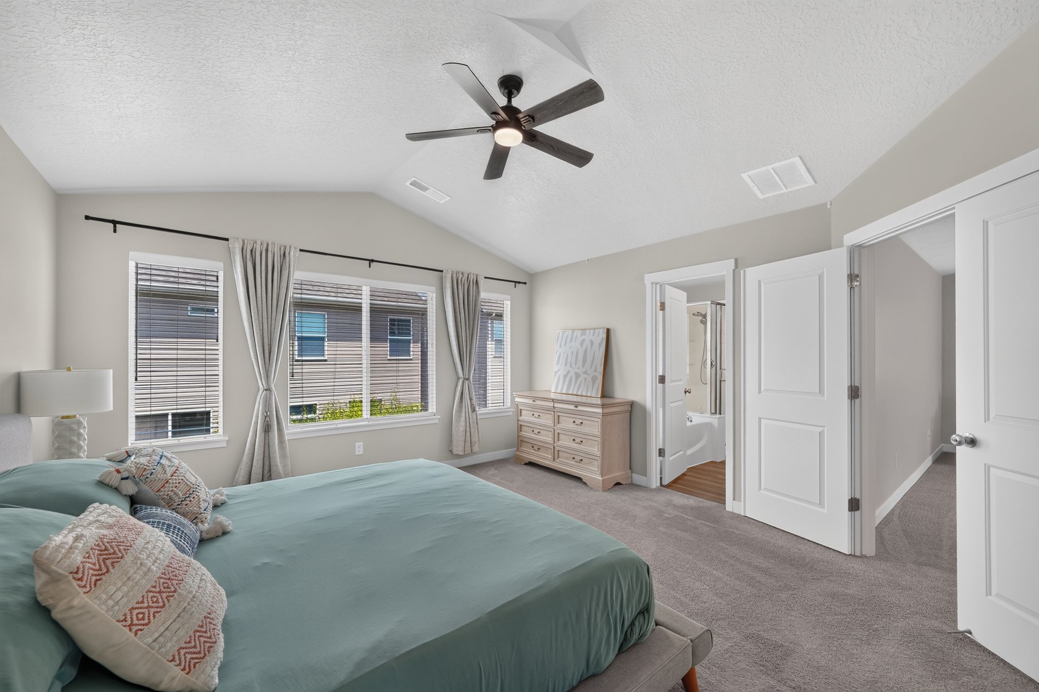 Spacious bedroom featuring vaulted ceilings, a ceiling fan with integrated lighting, and multiple windows with blinds