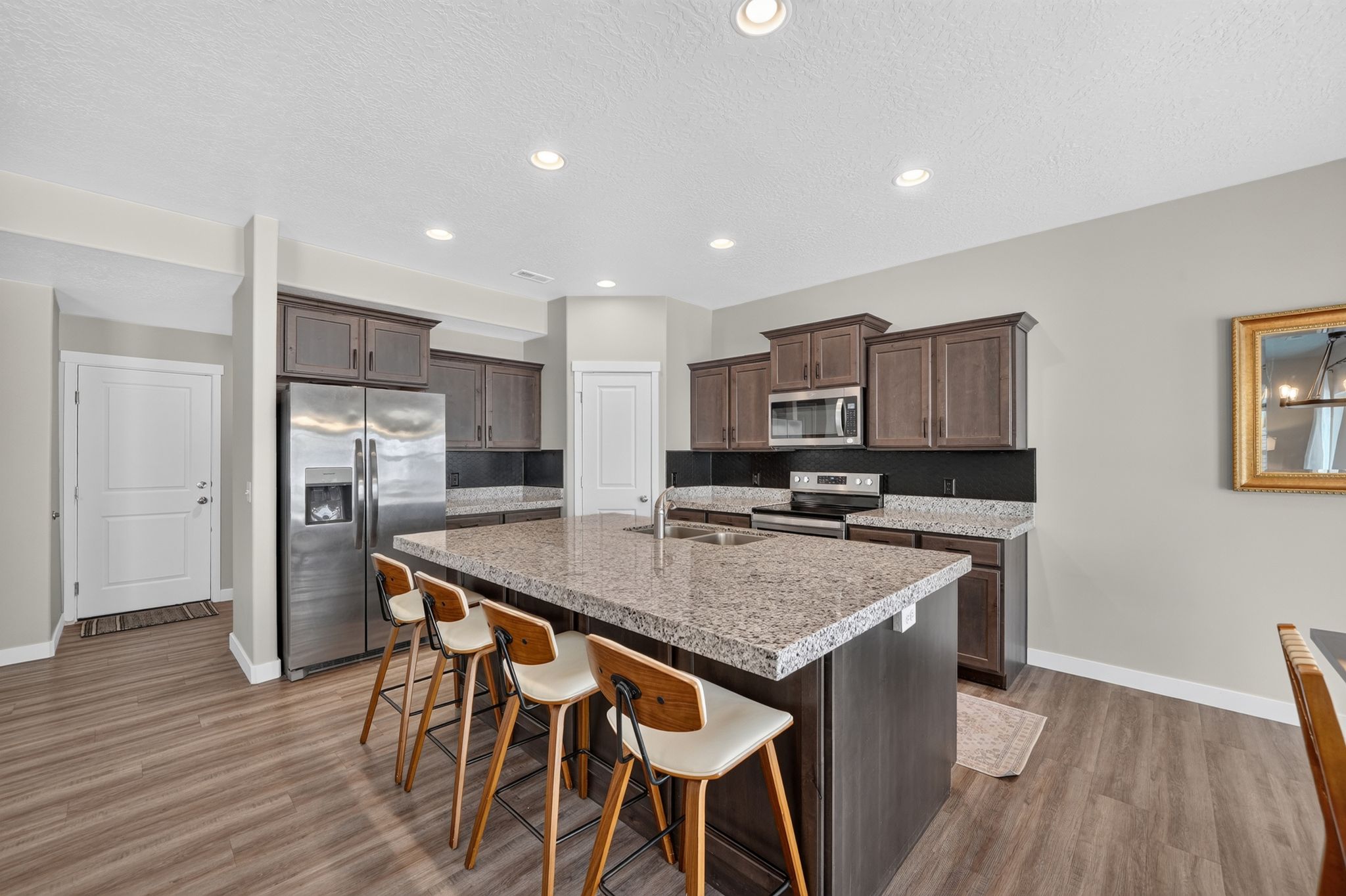 Spacious kitchen featuring an expansive island with a stone-finish countertop, stainless steel appliances, wood-finish flooring, recessed lighting, and dark wood cabinetry