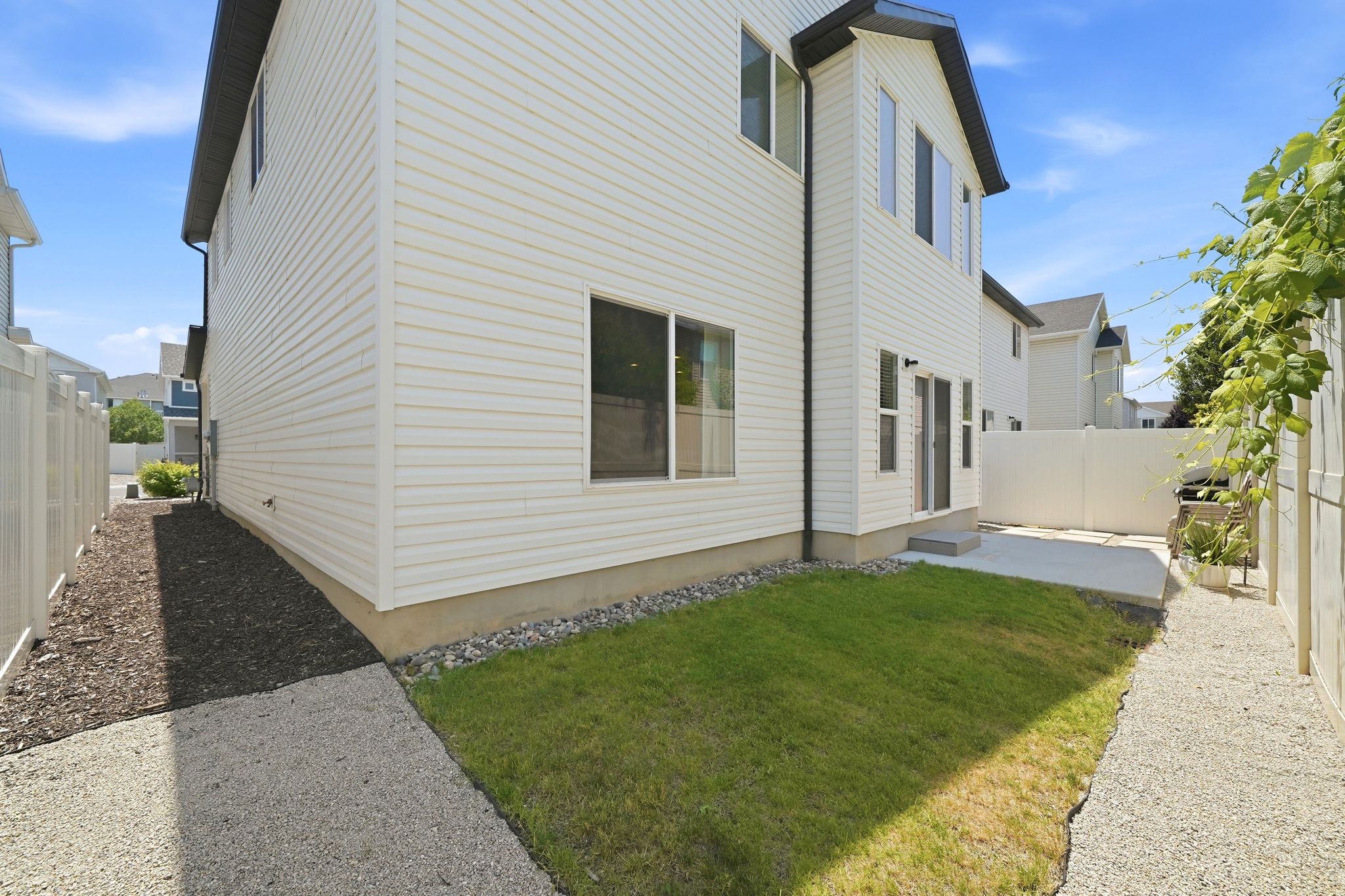 Rear exterior featuring white vinyl siding, a concrete patio, a small lawn area, and a privacy fence