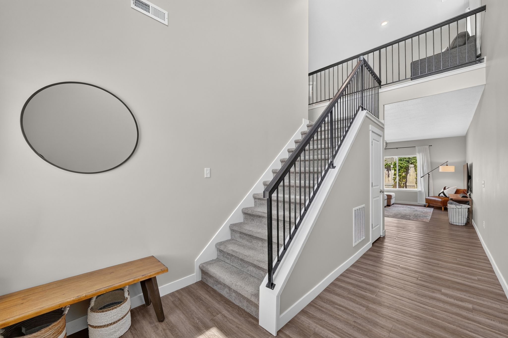 Two-story entryway featuring wood-finish flooring, a carpeted staircase with black iron railings, and a prominent second-story landing overlooking the space