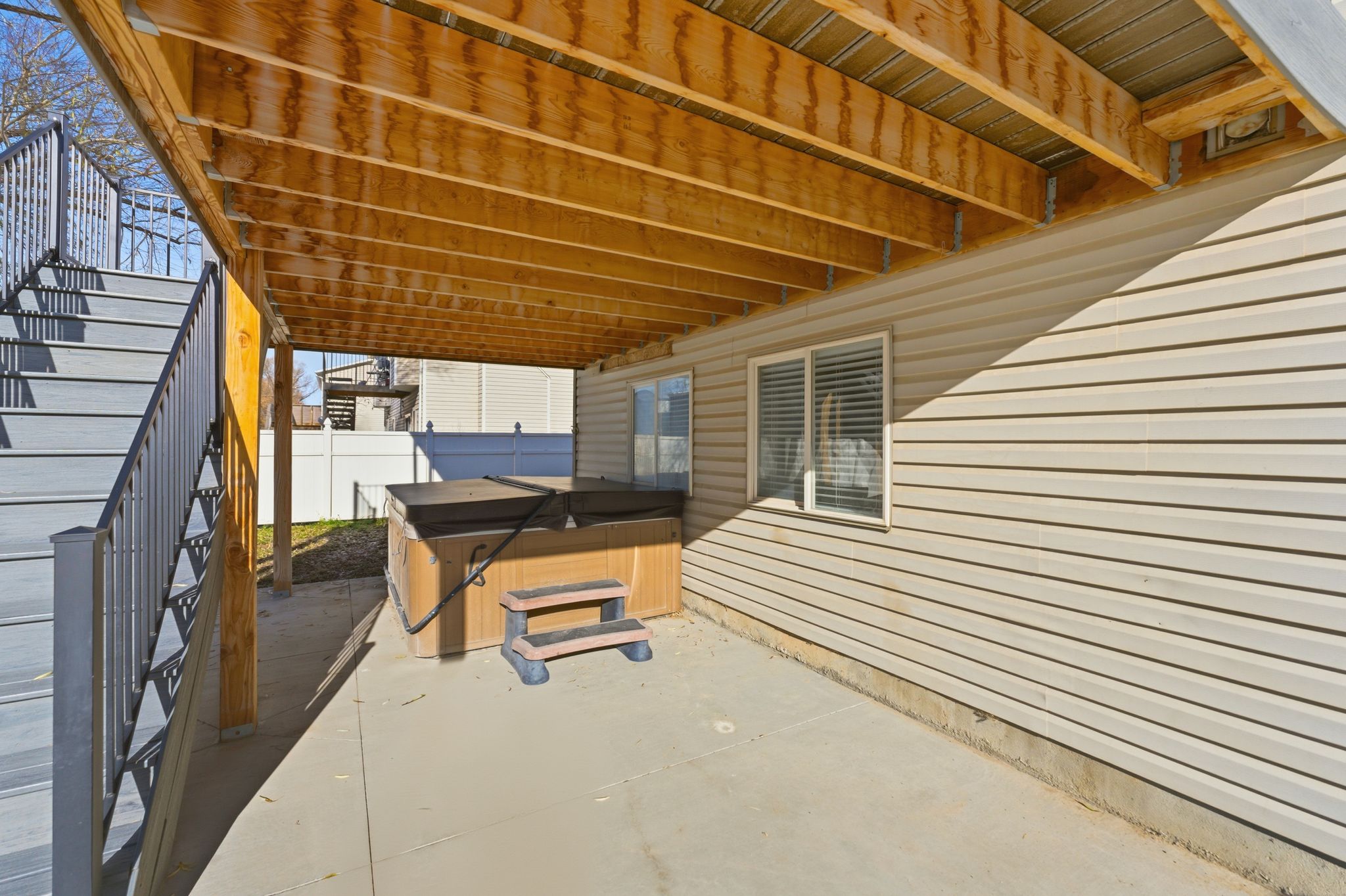 Covered patio area with concrete flooring, accented by a light-colored vinyl siding exterior and a finished wood ceiling
