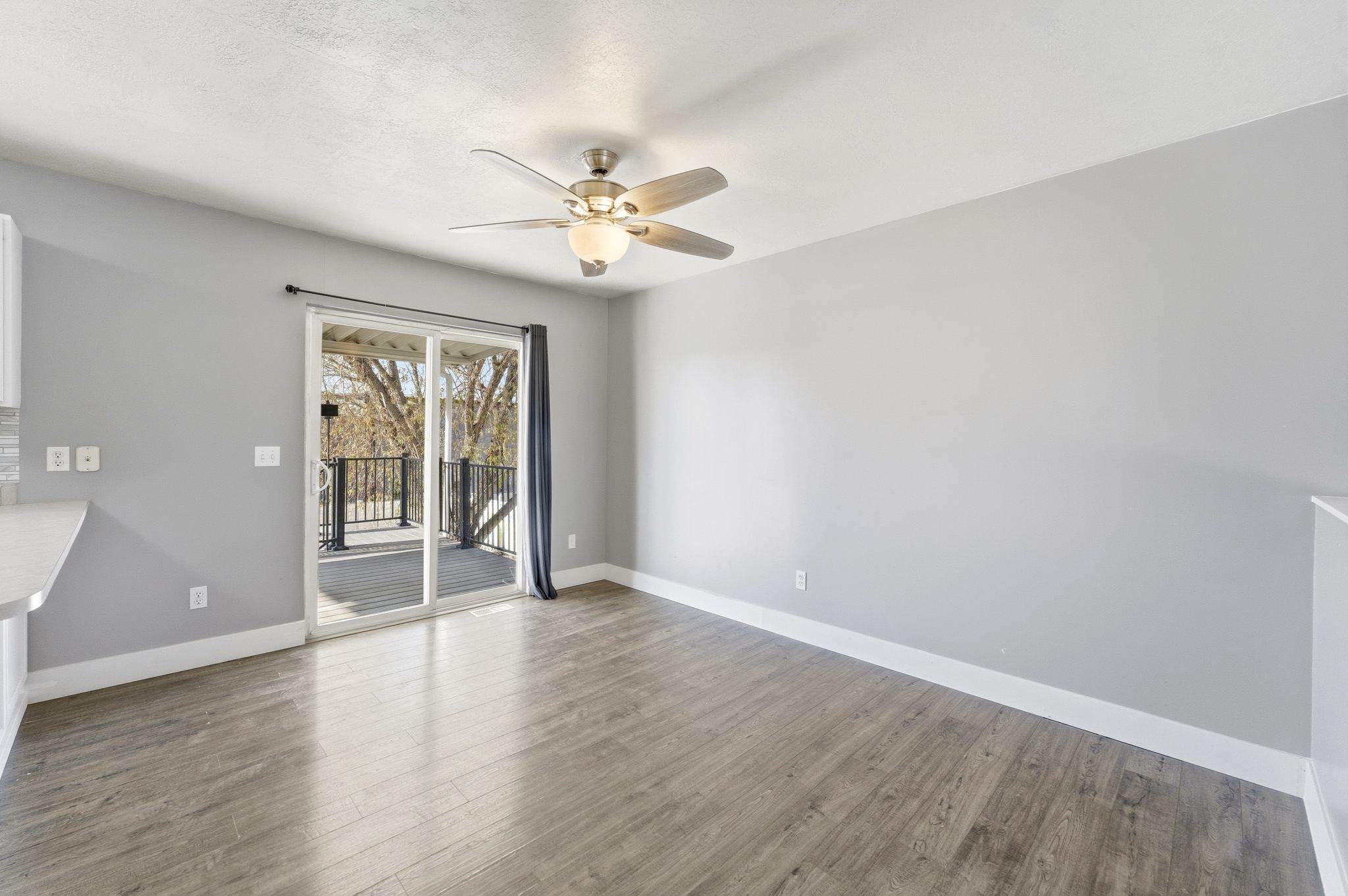 Spacious room featuring wood-finish flooring, light grey walls, and a ceiling fan with integrated lighting