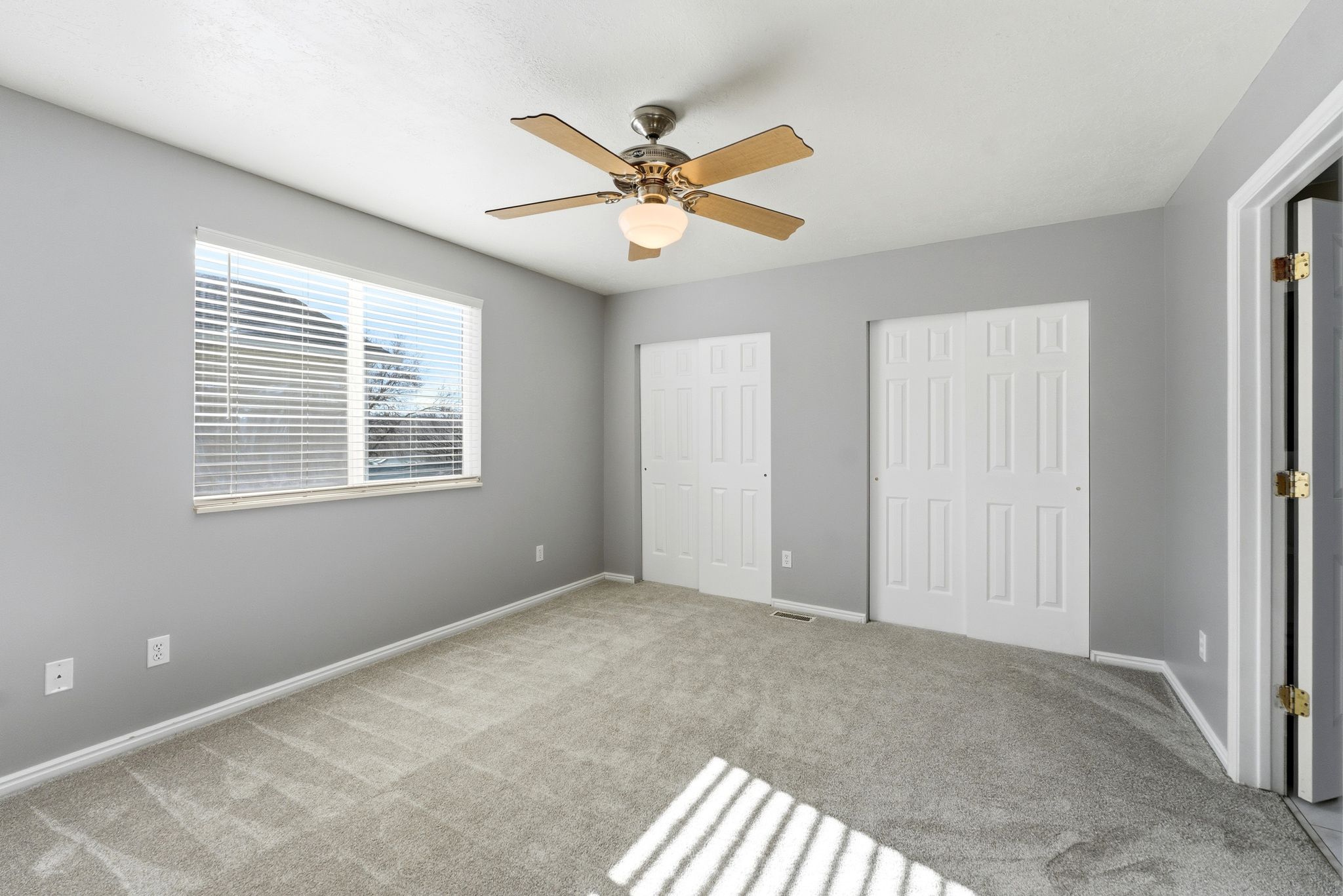 Carpeted room with a ceiling fan, a window featuring blinds, and two bi-fold closet doors