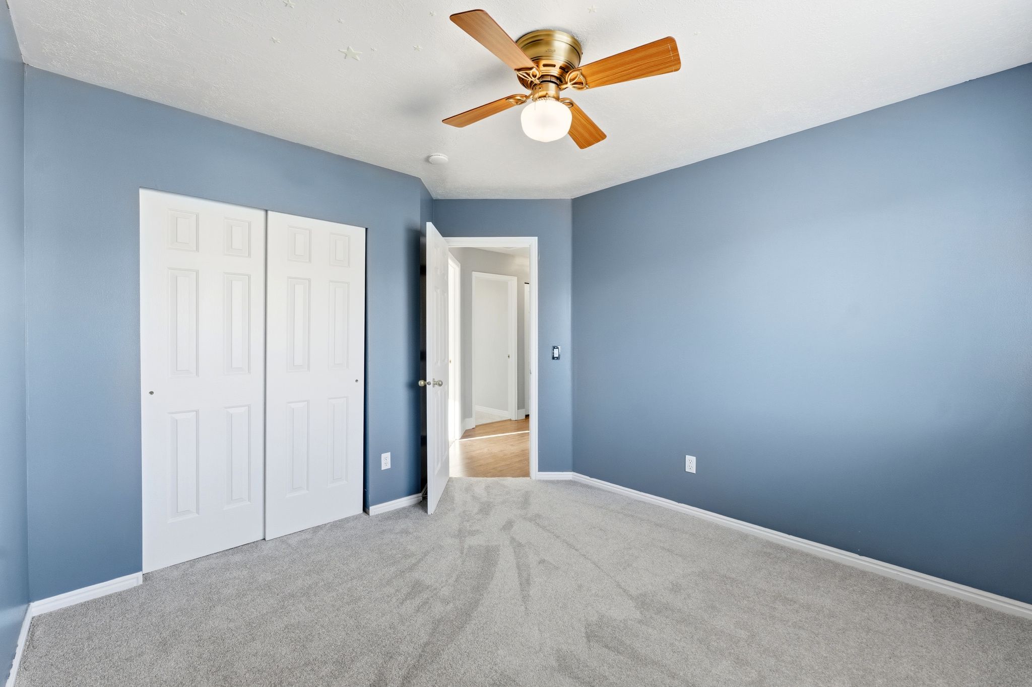 Bright room with blue walls, light gray carpet, and a brass-finish ceiling fan with wood-finish blades