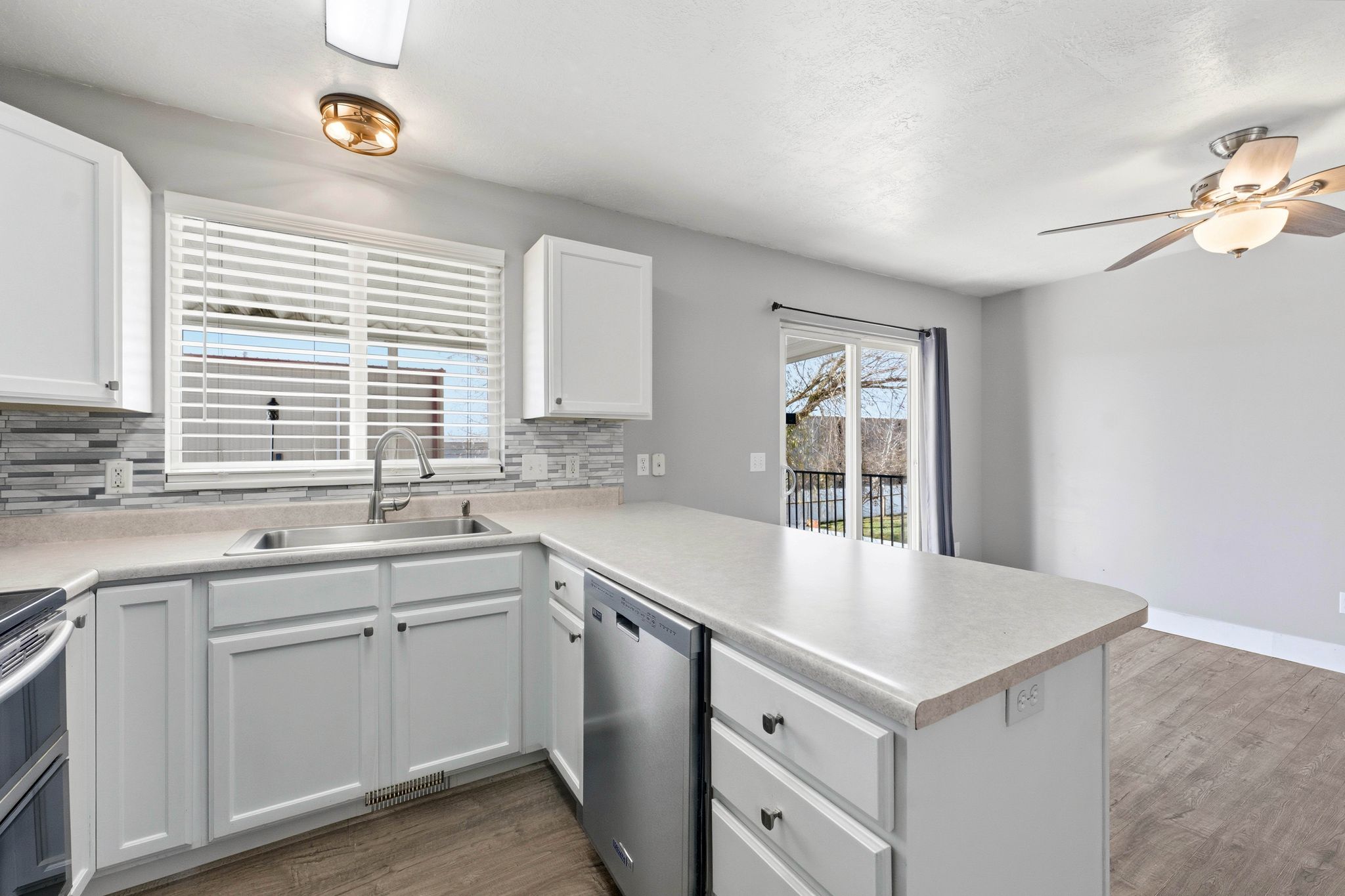 Contemporary kitchen featuring white cabinetry, a stainless steel double basin sink with a gooseneck faucet, light-toned countertops, and a mosaic tile backsplash