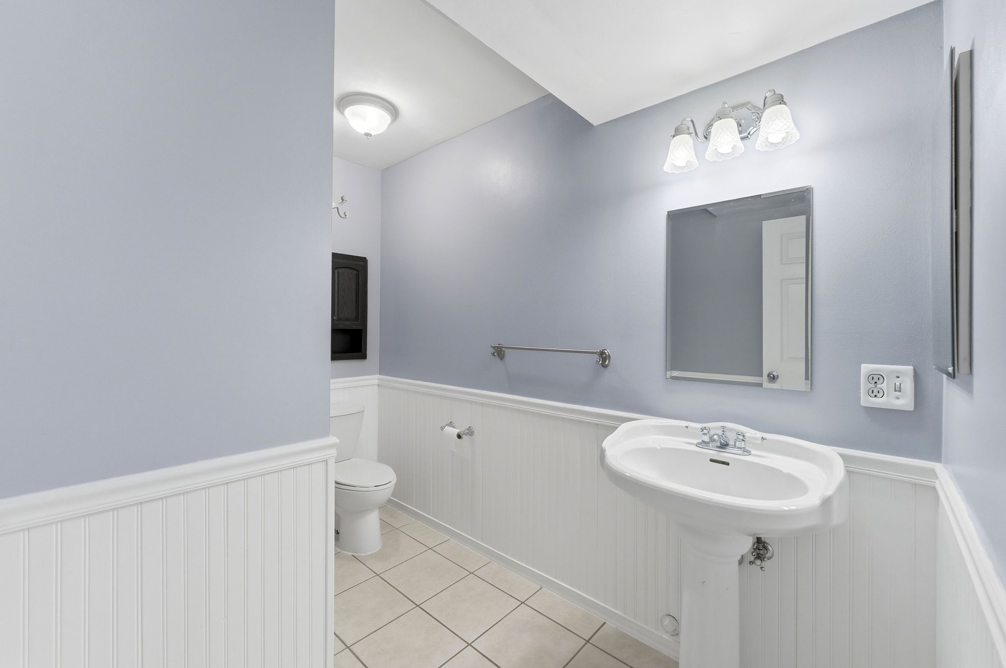 Pedestal sink with chrome faucet, square mirror, and three-light vanity fixture