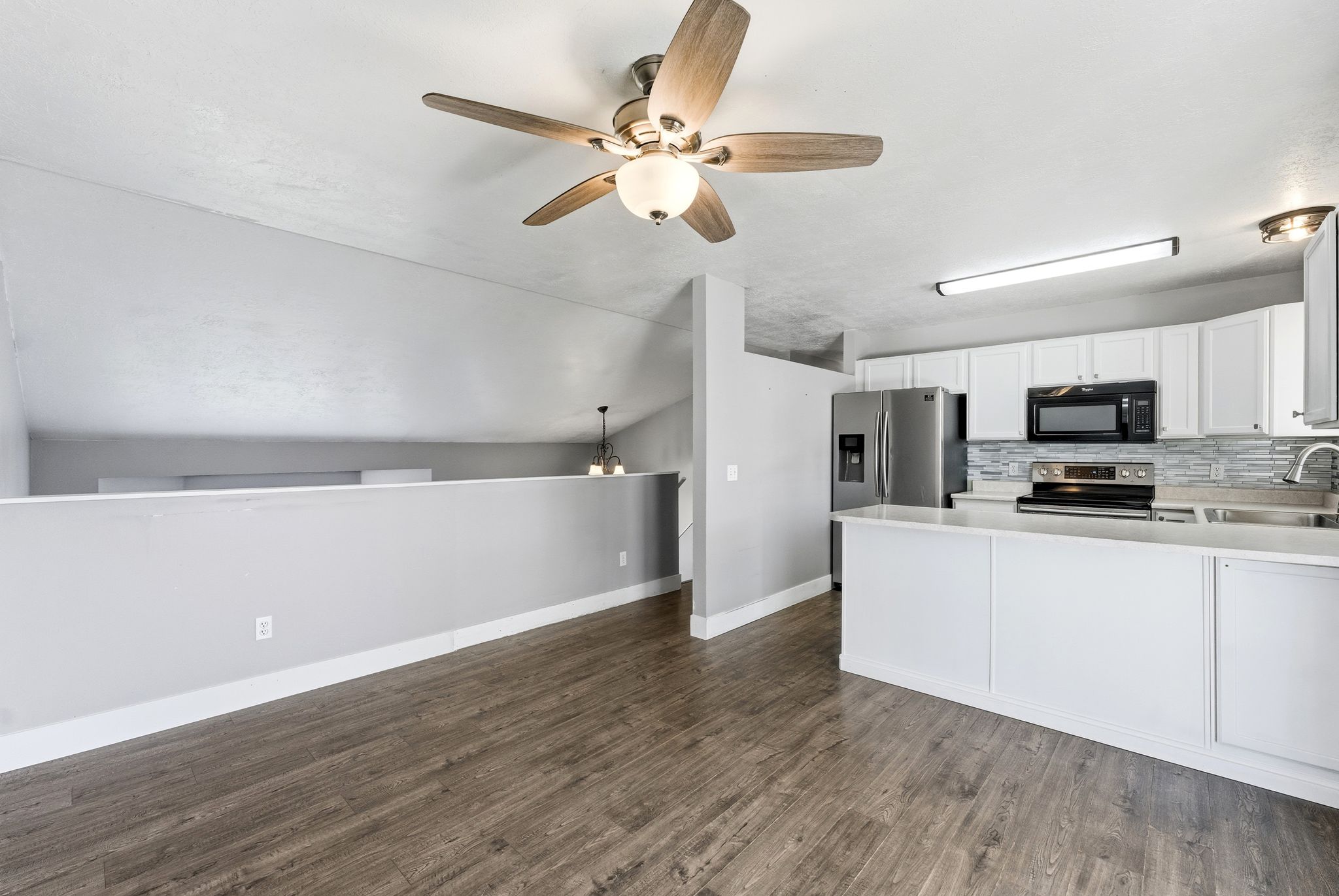 Open-concept living space featuring wood-finish flooring, a contemporary ceiling fan, and a kitchen with white cabinetry, stainless steel appliances, and a tiled backsplash