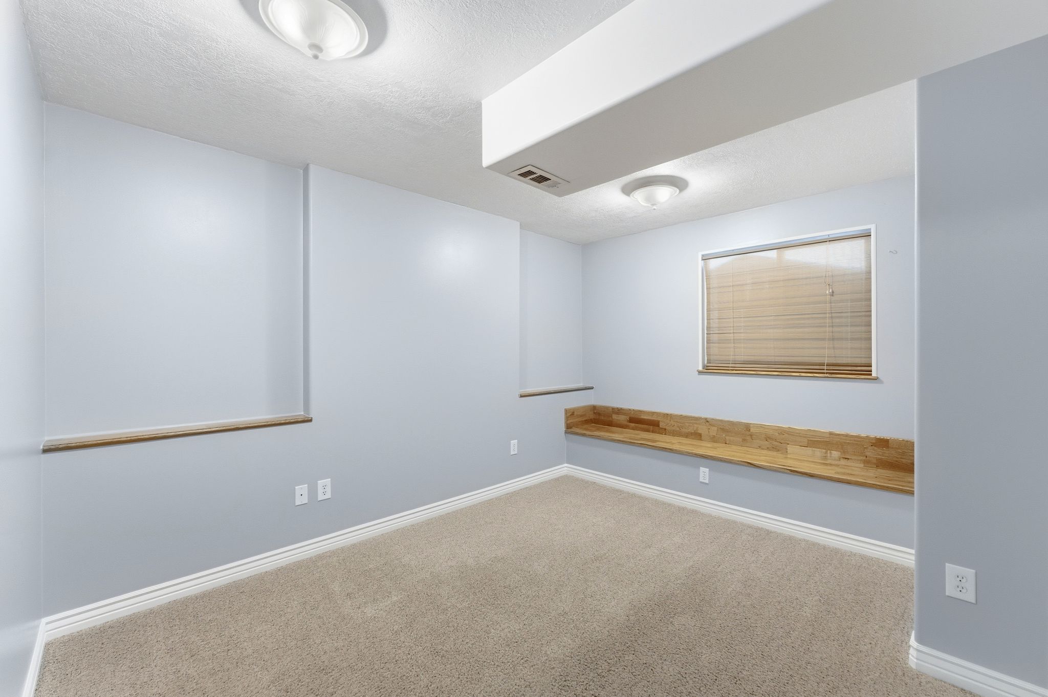 Carpeted room featuring light blue walls, white trim, and a built-in wood-finish bench below a window with horizontal blinds