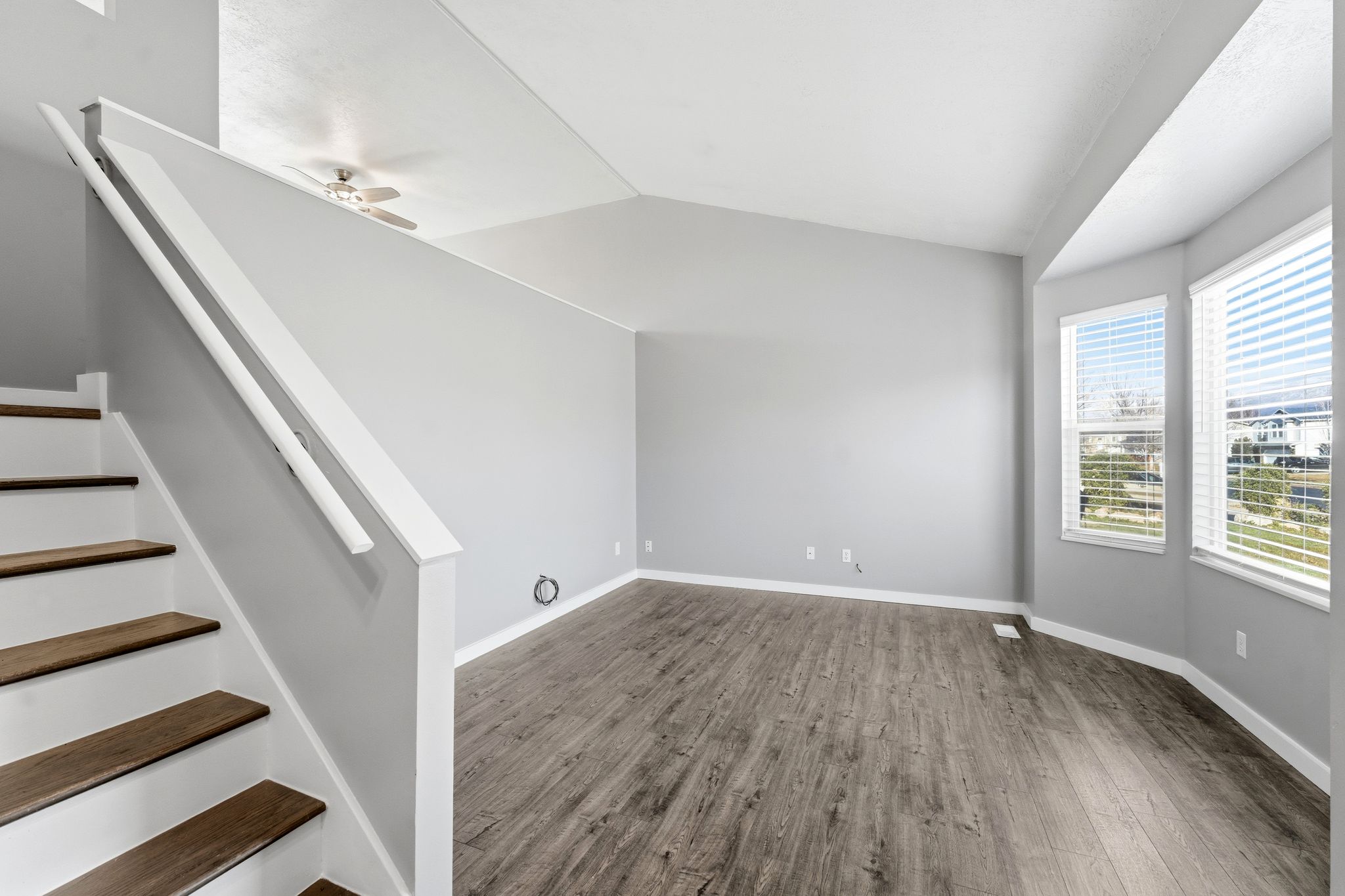 Spacious living area featuring wood-finish flooring, vaulted ceilings, and a bay window with natural light