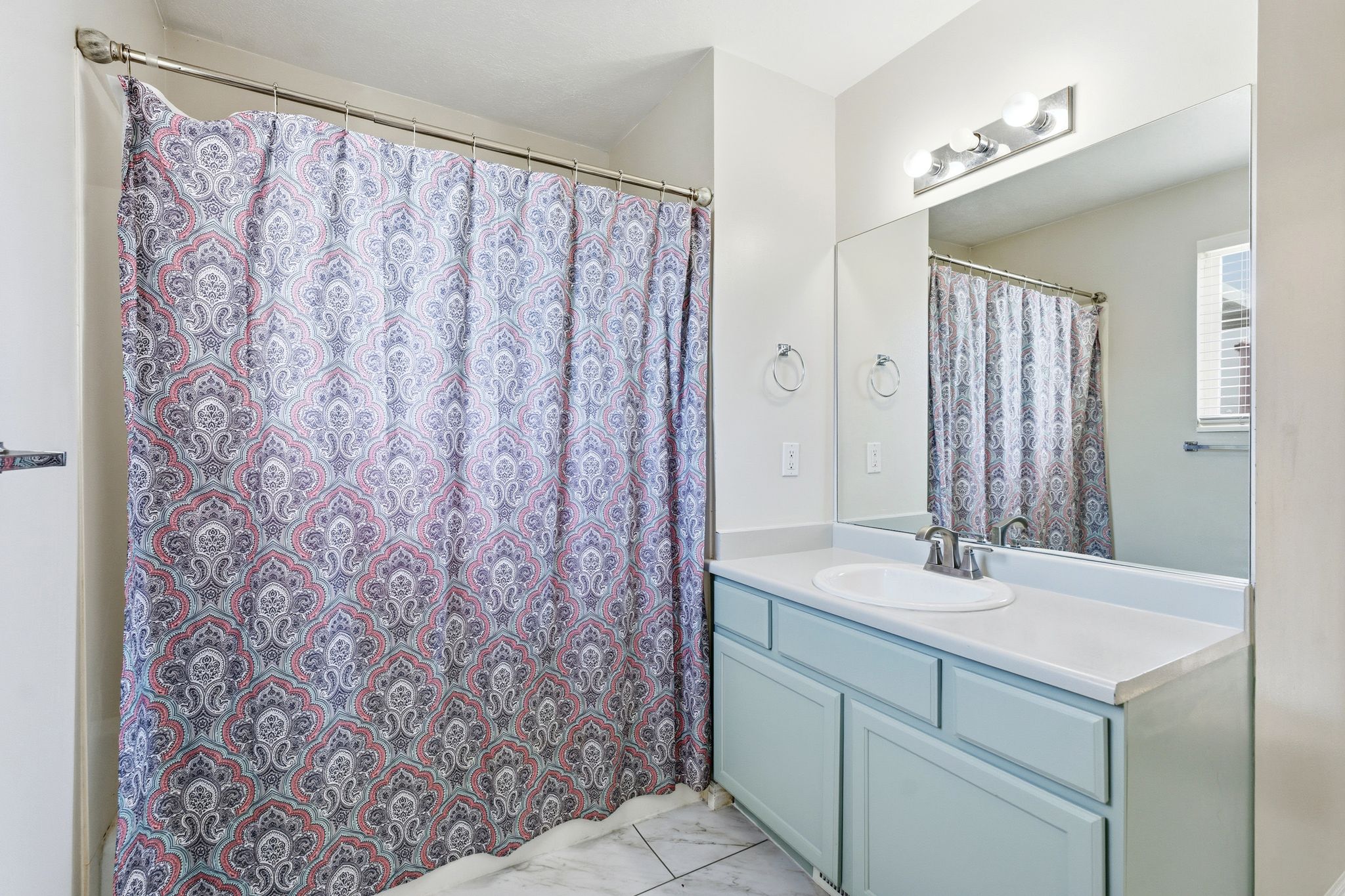 Bathroom featuring a single vanity with light blue cabinetry, an integrated sink, and a large wall-mounted mirror