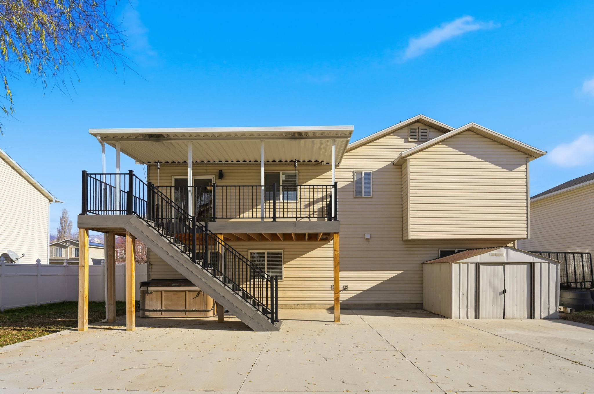Rear exterior featuring a covered deck with black railings, exterior stairs, a concrete patio, and a storage shed
