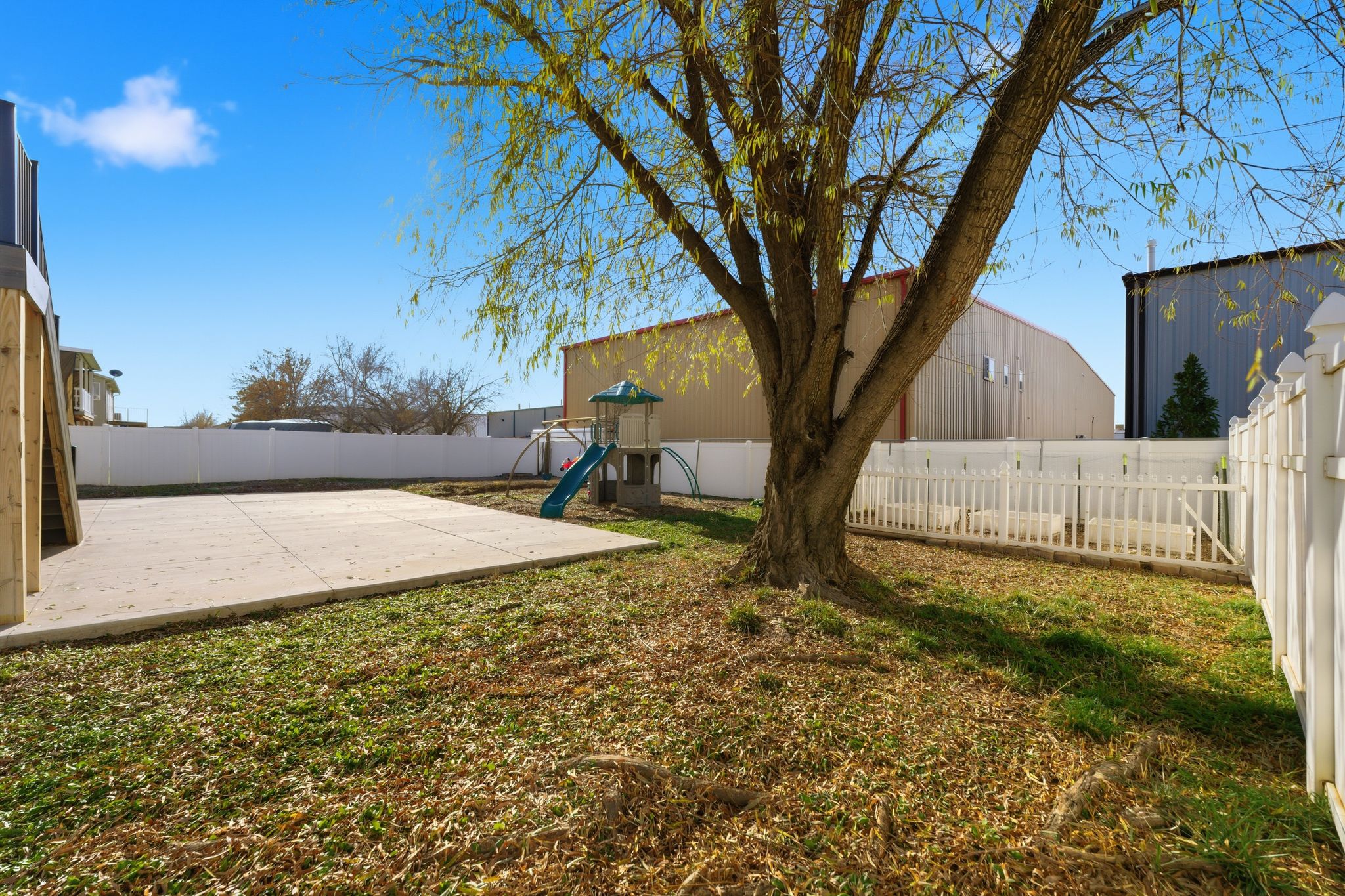 Expansive grassy yard featuring a substantial tree and a concrete patio