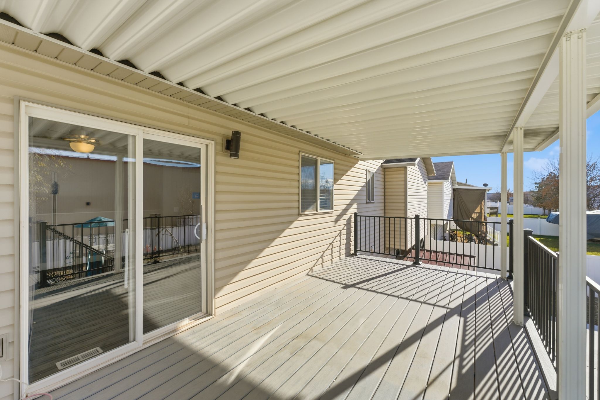 Covered deck featuring composite decking, white vinyl siding, a sliding glass door, and black metal railings