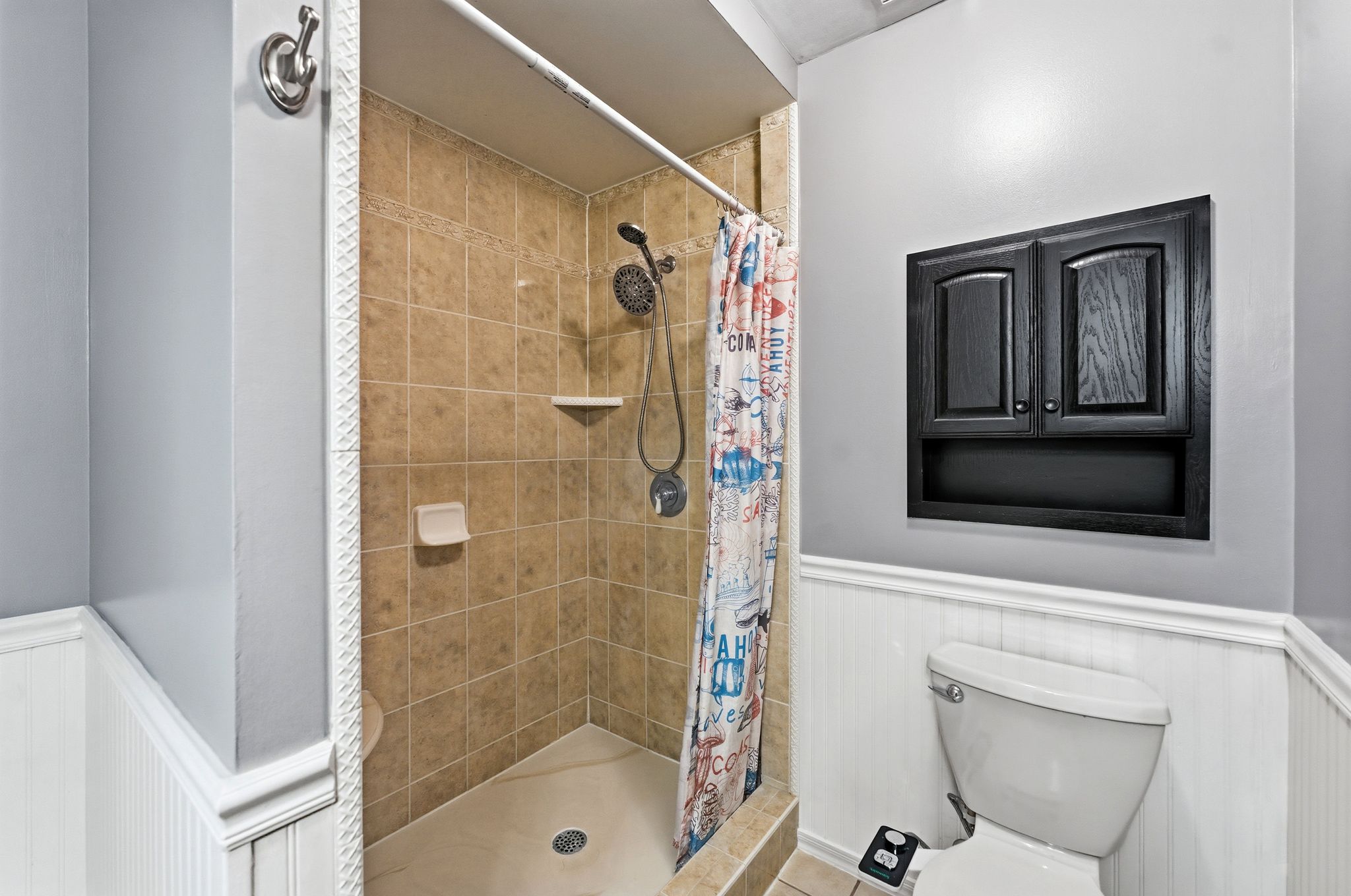 Tiled shower enclosure with built-in shelving, complemented by a recessed wall cabinet with arched panel doors