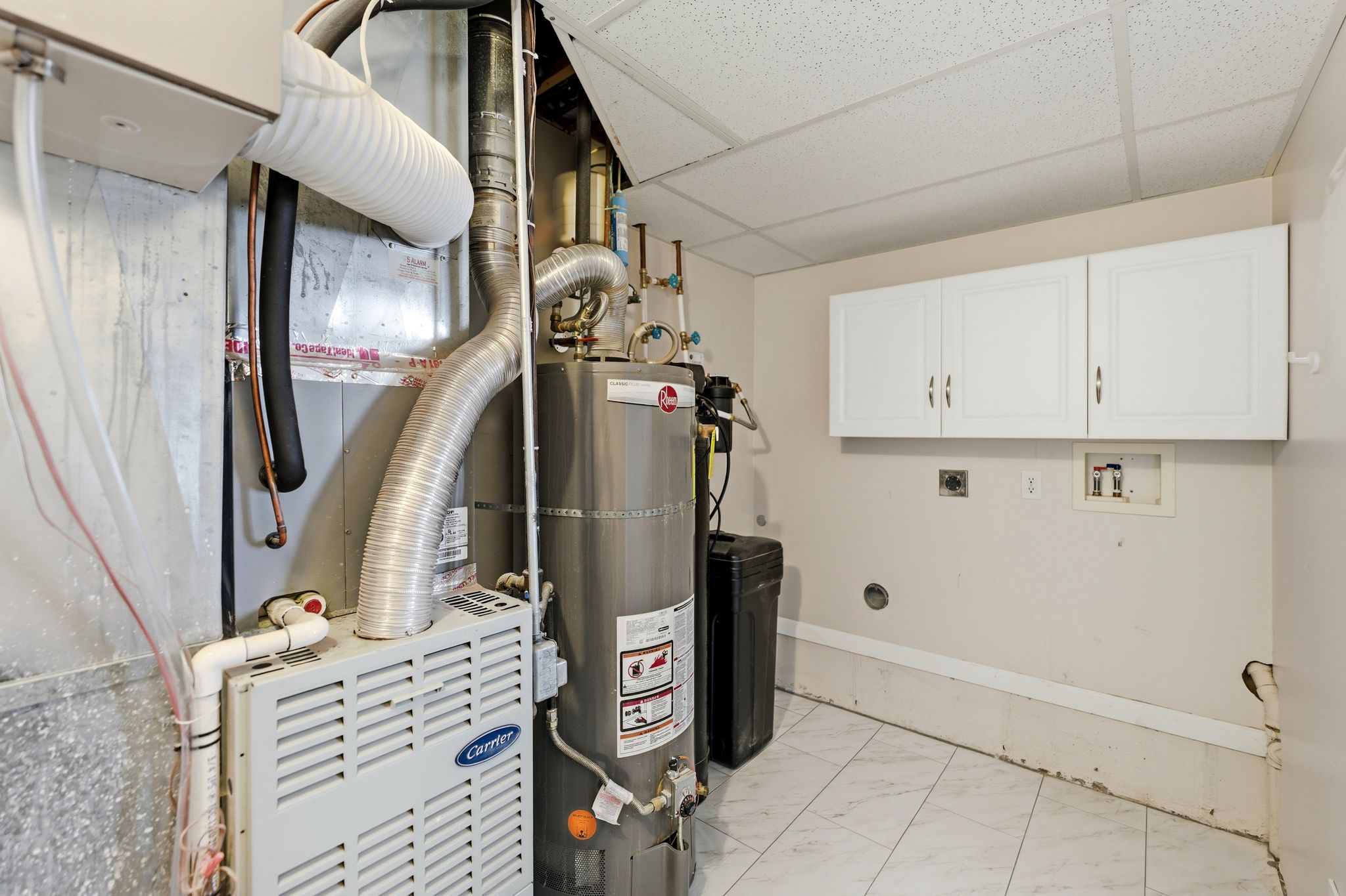 Utility area featuring a water heater, furnace, and white overhead cabinetry