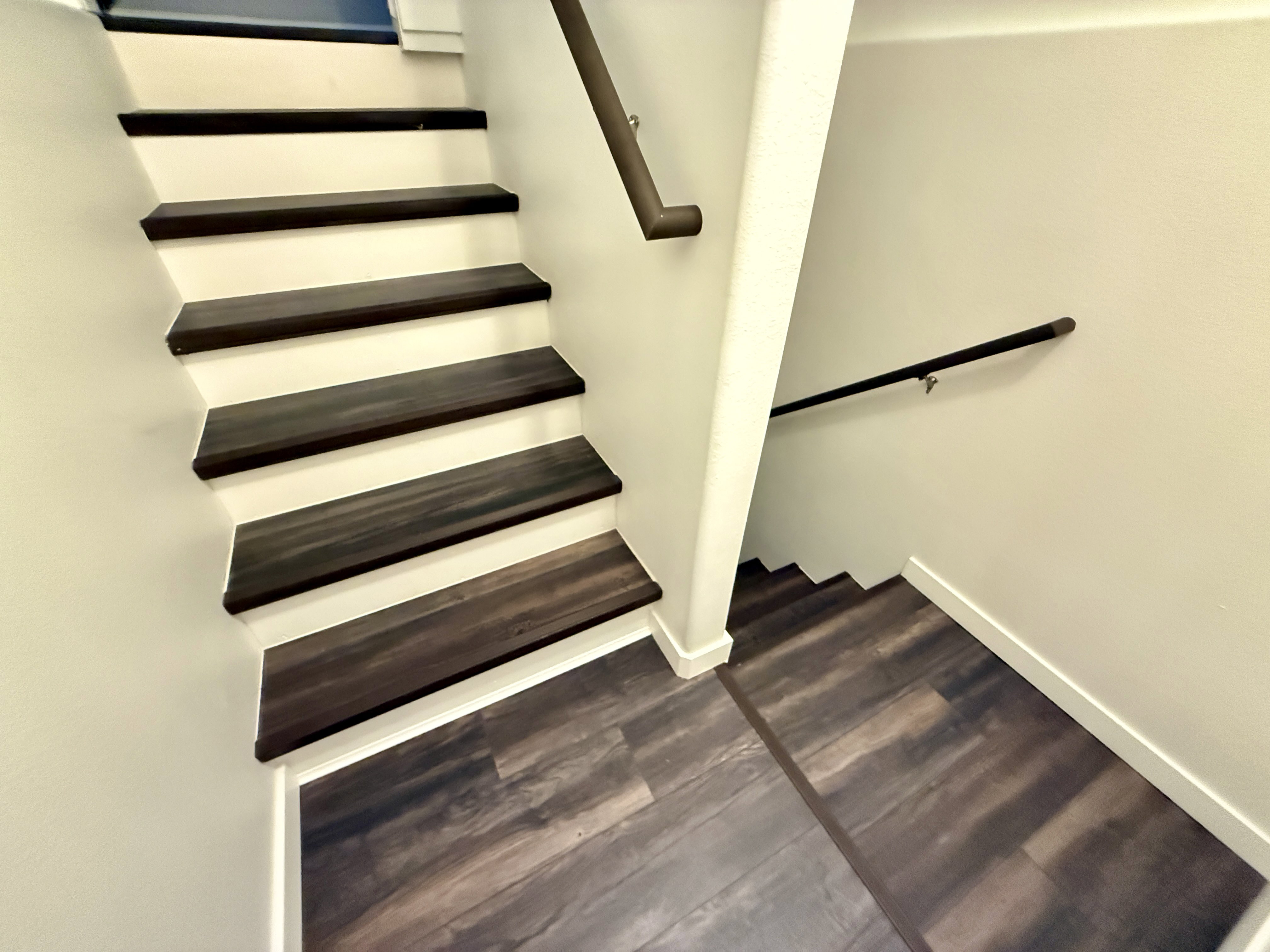 Multi-level staircase featuring dark wood-finish treads and risers, coordinating wood-finish flooring, and a dark-toned handrail