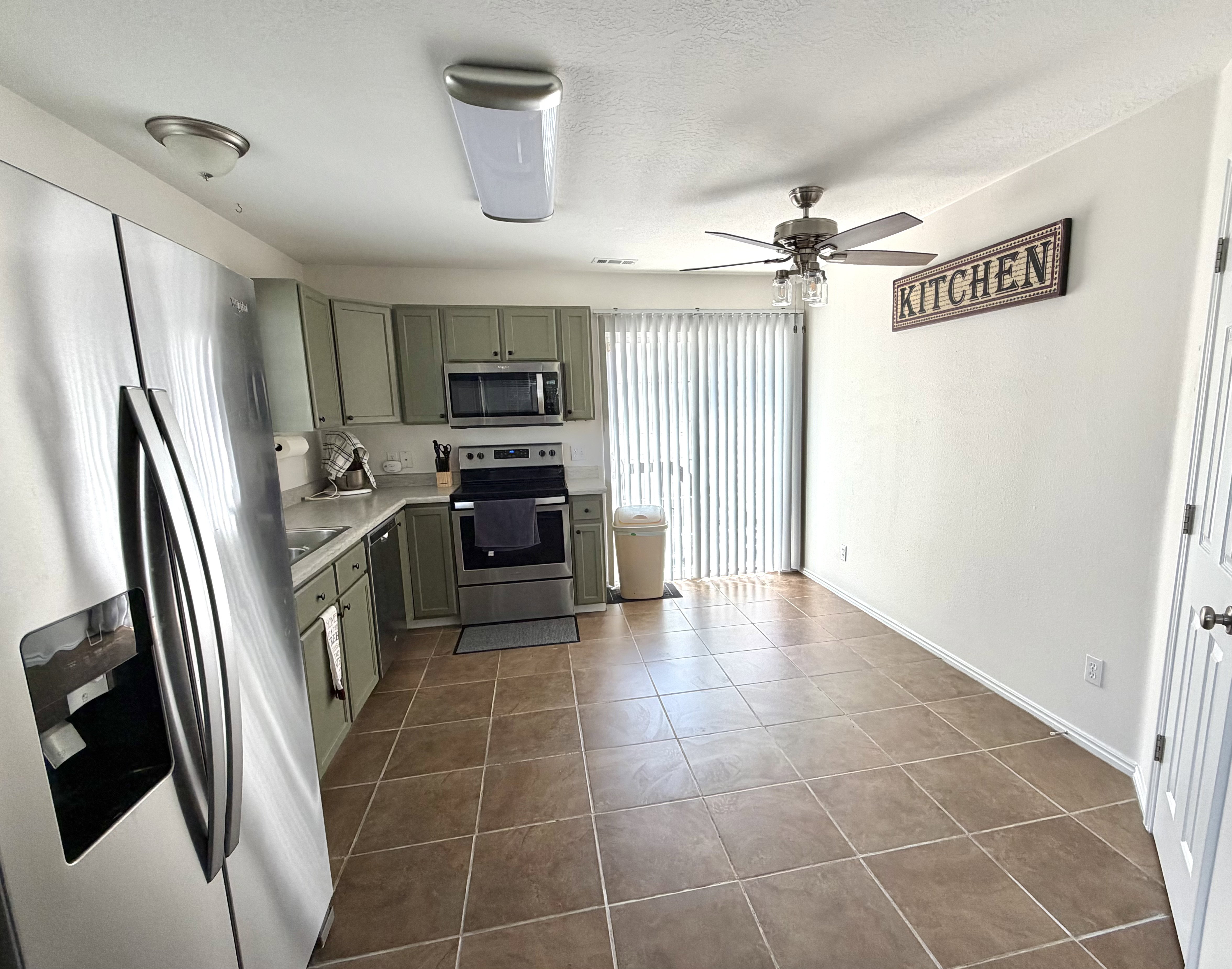 Kitchen featuring stainless steel appliances, sage green cabinetry, a ceiling fan with light, and sliding glass door with vertical blinds