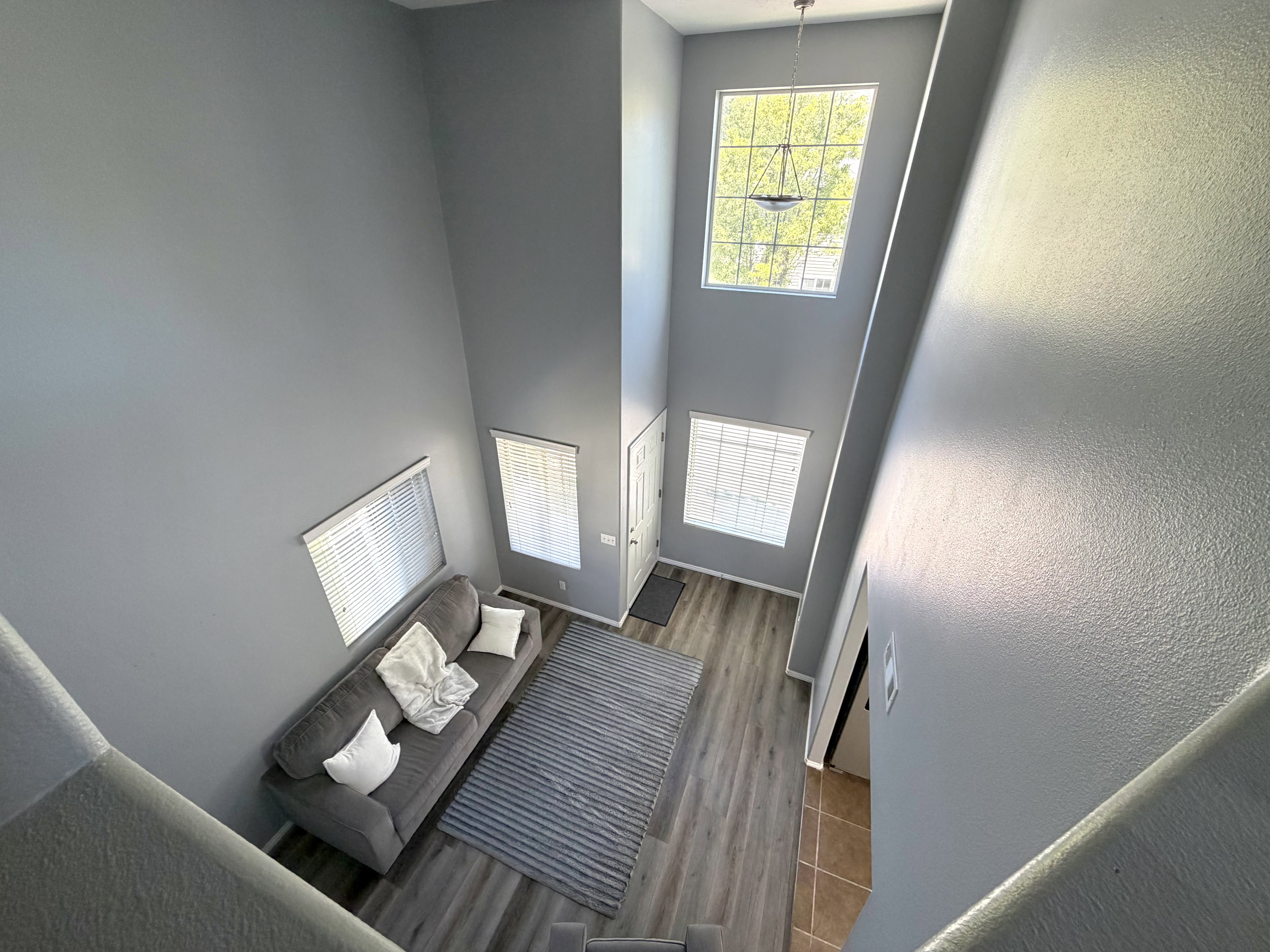 Two-story entryway with vaulted ceilings, large picture windows, wood-finish flooring, and a decorative chandelier