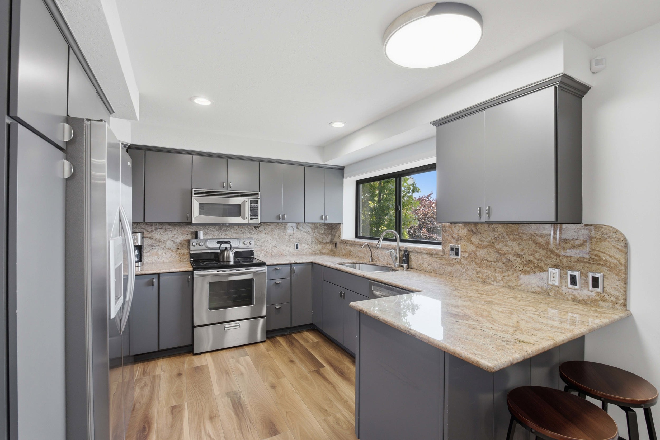 Kitchen featuring grey cabinetry, stainless steel appliances, granite countertops with a matching backsplash, wood-finish flooring, and a built-in breakfast bar